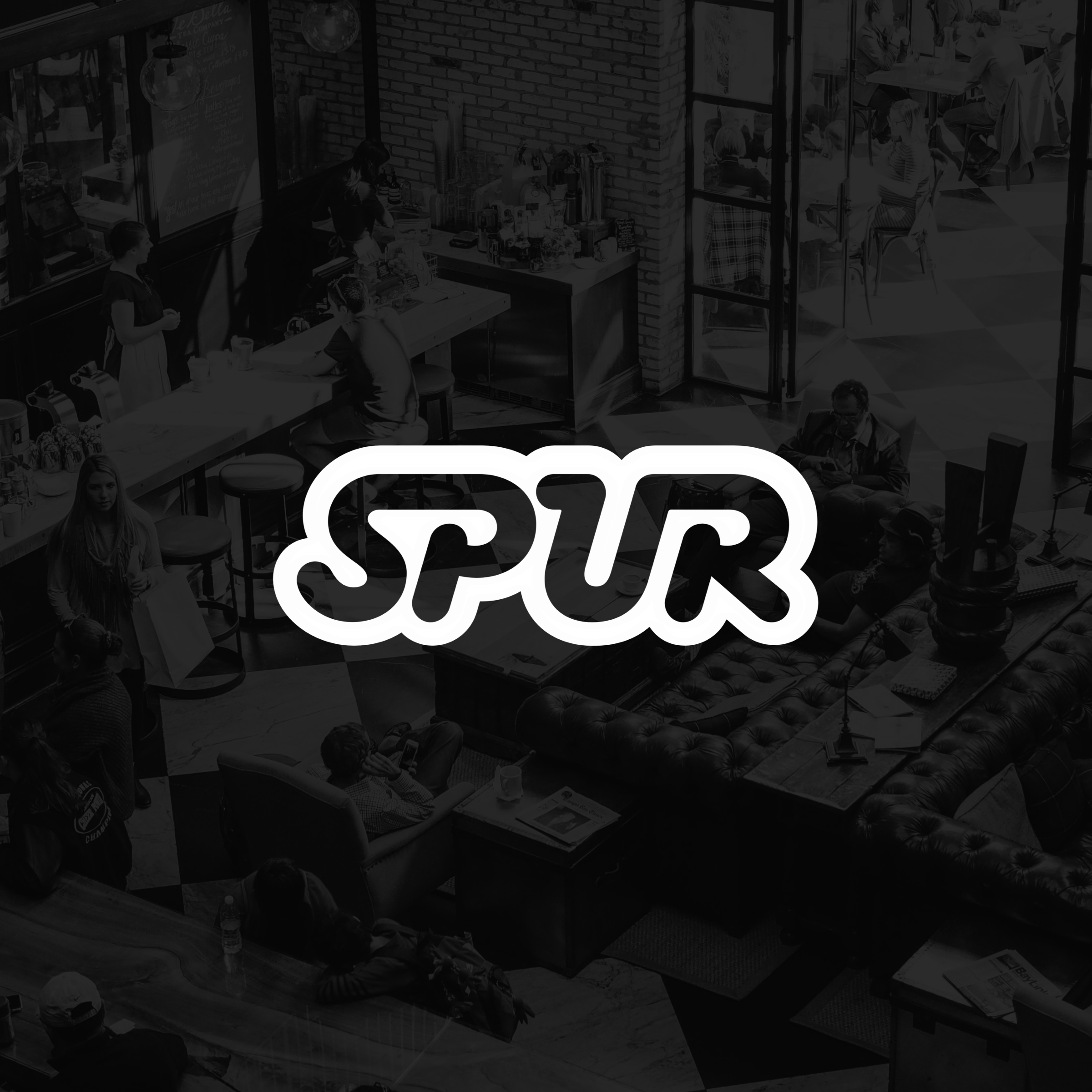 A black and white photo of a coffee shop interior with people sitting at tables and chairs, some waiting in line at the counter, and the SPUR logo prominently displayed in the center.