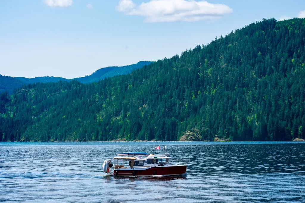 A red and white boat on a calm body of water with green forested hills in the background.
