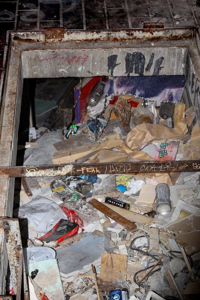 Rusty and dirty building debris with trash, paper, cans, and broken materials scattered throughout.