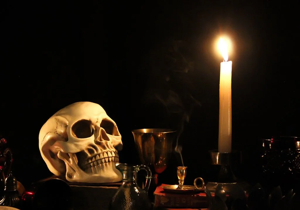 A lit candle, skull, and various metallic objects on a dark background.