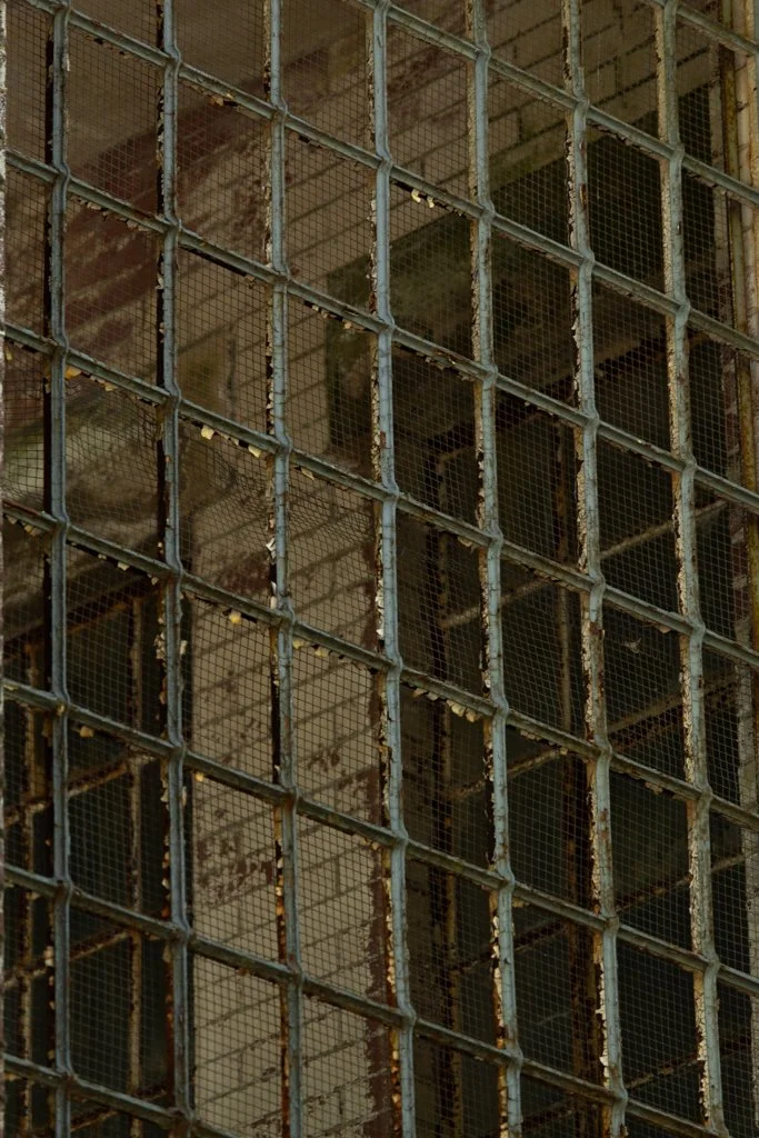 Close-up of a rusted metal framework with small wire mesh squares, possibly part of an old building or industrial structure.