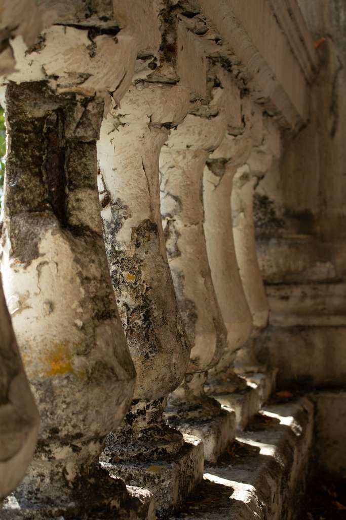 Close-up of worn and weathered stone balusters with light filtering through gaps, showing moss and dirt buildup.