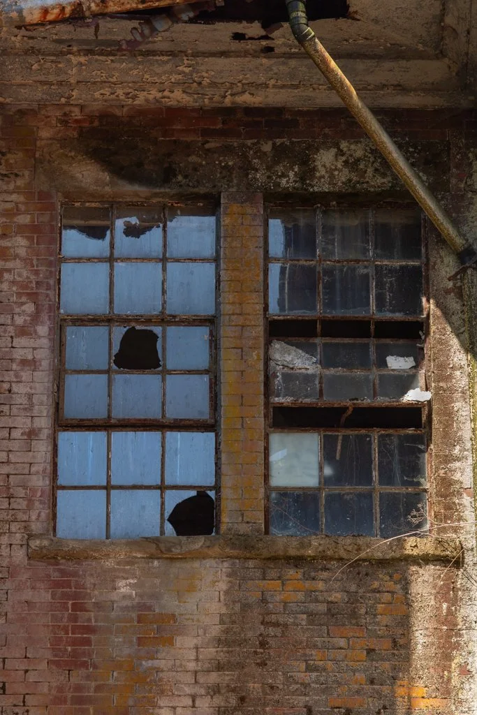 Broken and dirty industrial window with rusted metal frame in an old brick building.