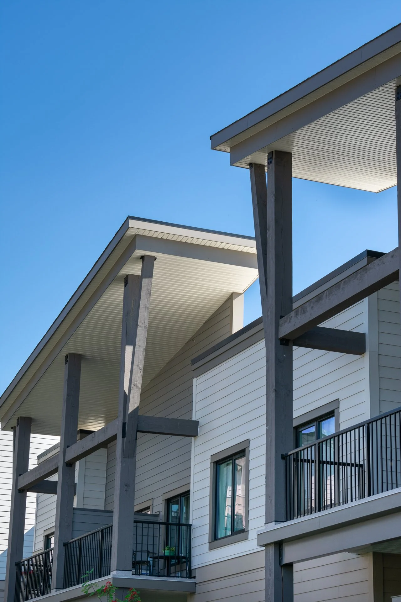 Exterior view of a modern residential building with angular roofs, white siding, and black metal railings on the balconies, under a clear blue sky.