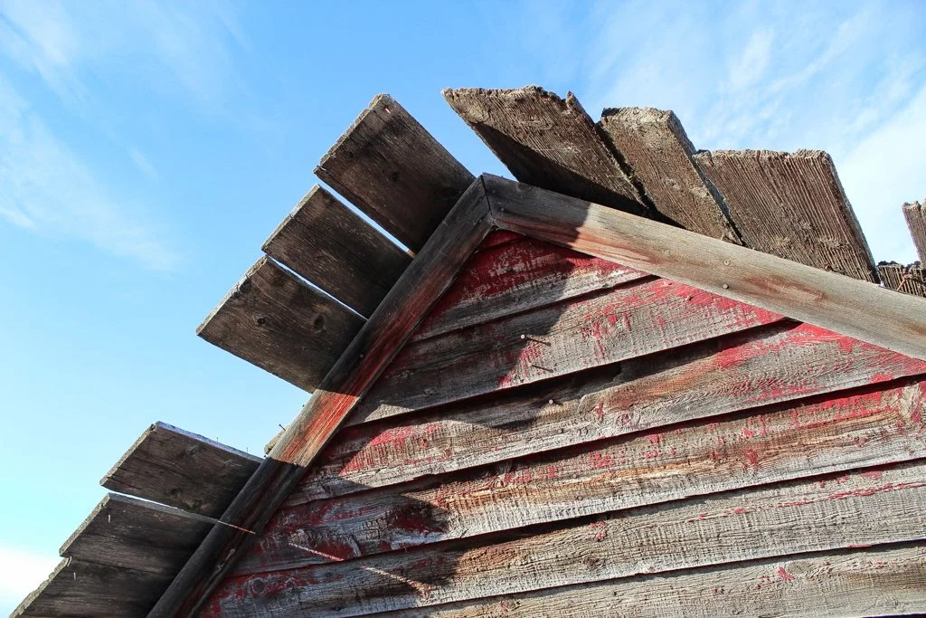 Close-up of weathered wooden planks and beams of an old shed or barn against a blue sky.