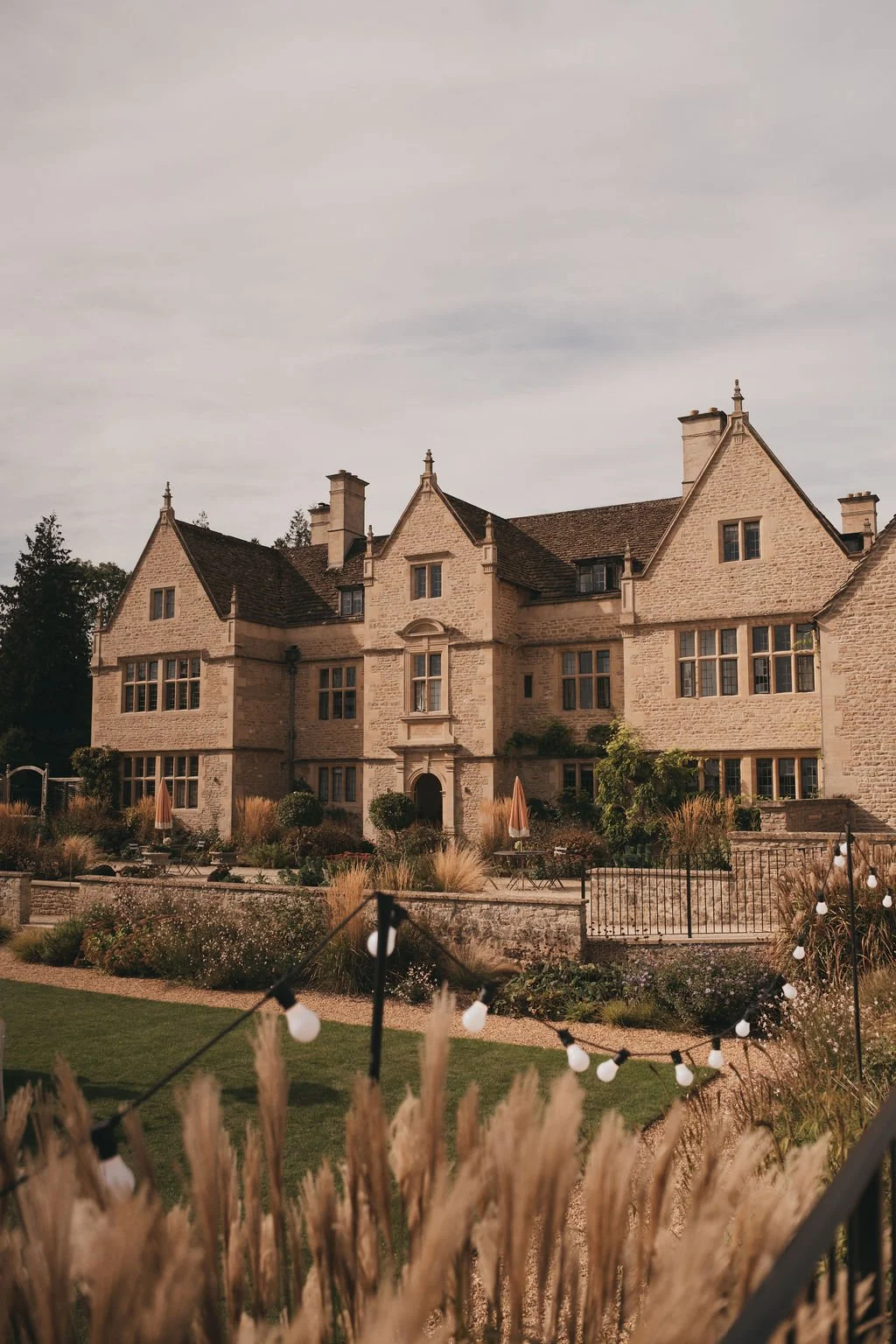 Kin House in Wiltshire, surrounded by beautiful gardens with plants, shrubs, and outdoor seating, under an atmospheric sky.