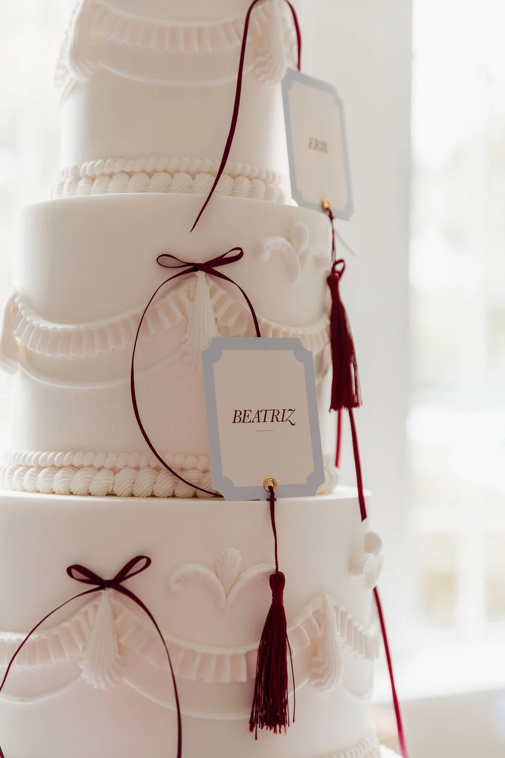 Luxury wedding place cards with burgundy tassels arranged alongside a stunning wedding cake. Place cards designed by Carrie at Honey Bee Mine, and captured in the Scottish Highlands.