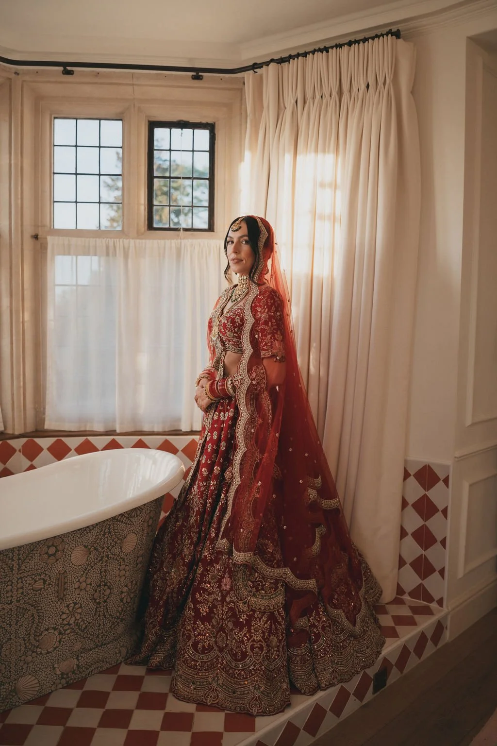 A woman dressed in a traditional red bridal outfit with intricate gold embroidery, standing in one of the bathrooms at Kin House.