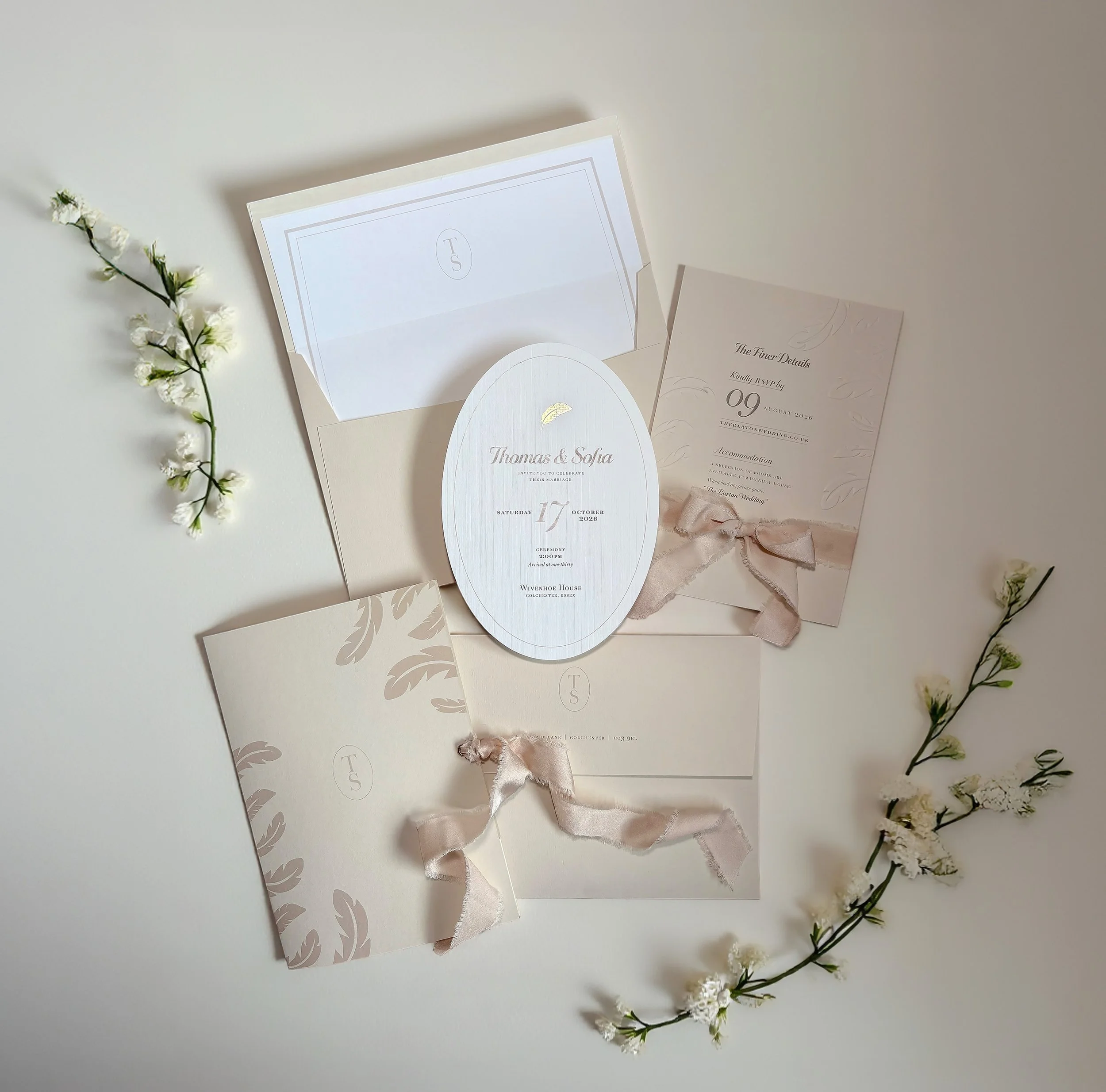 Fashion-forward invitation suite showing pocket-fold wrap with monogram and champagne silk ribbon, with oval die-cut invitation, gold foil details and delicate embossing. From the La Plume wedding stationery collection by Honey Bee Mine.