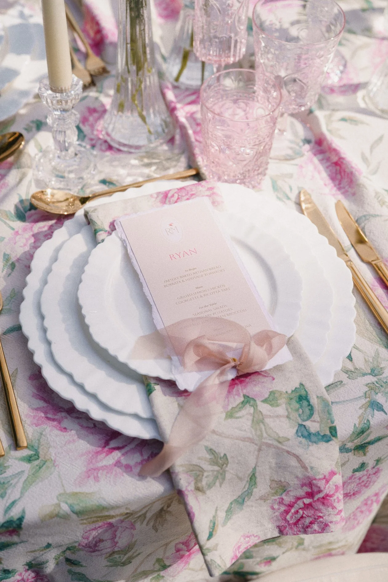 Blush pink wedding menu styled on a floral tablescape with scalloped plates and pink glassware – designed by Honey Bee Mine.