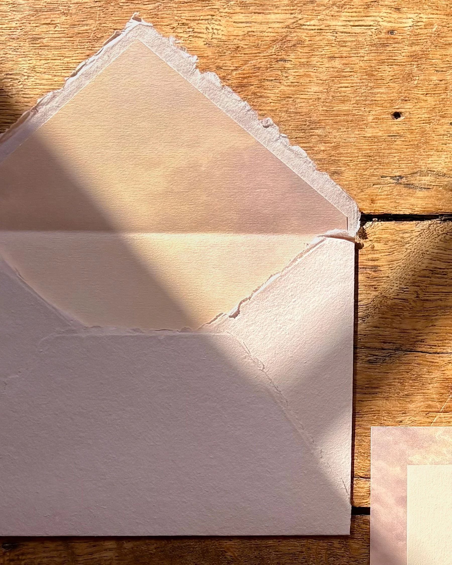 Layered die-cut wedding invitations in soft rose and warm ivory with ribbon detailing and handmade paper envelope