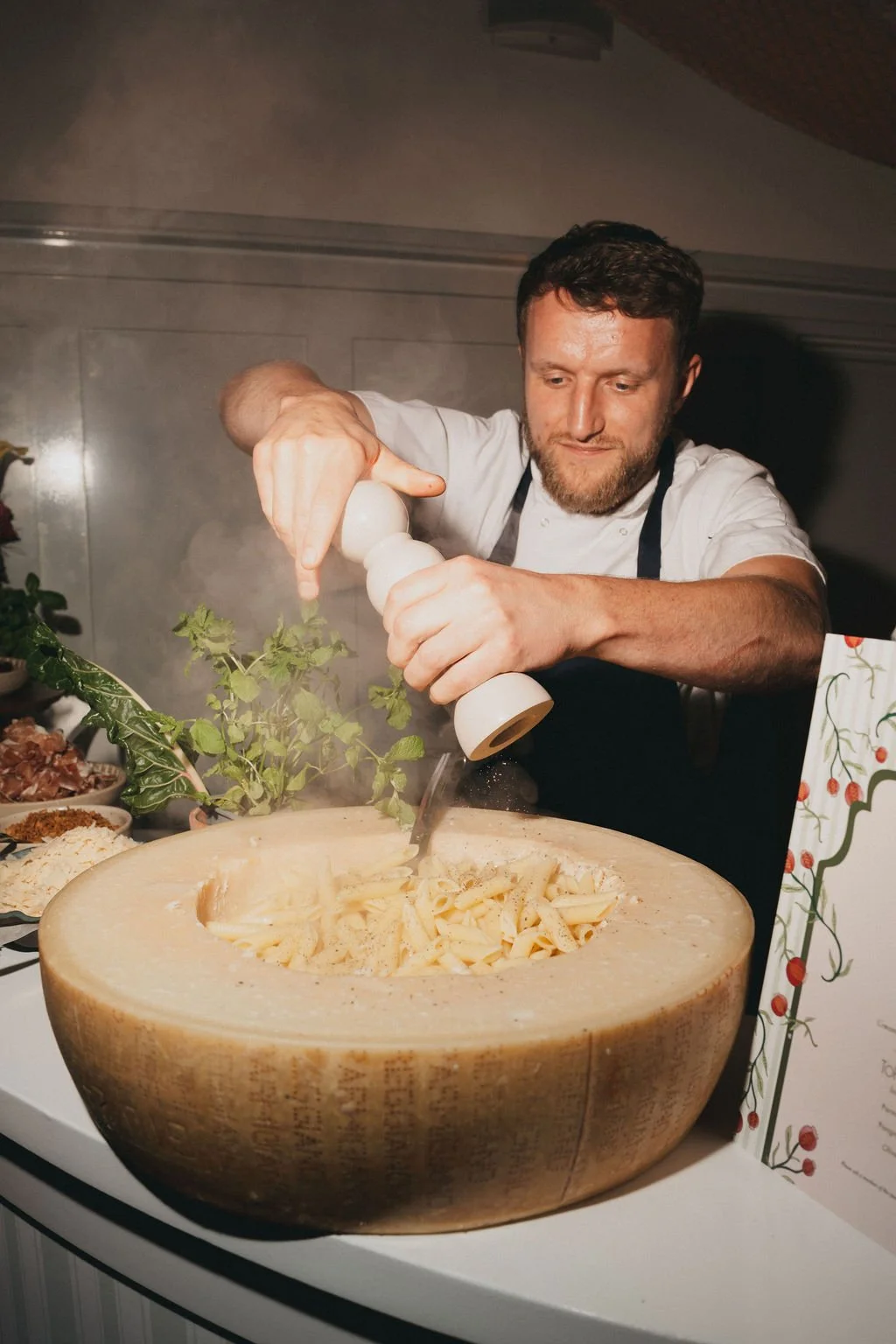 A chef grating cheese into a large wheel of cheese used as a serving bowl for pasta, for a multi-day wedding at Kin House.