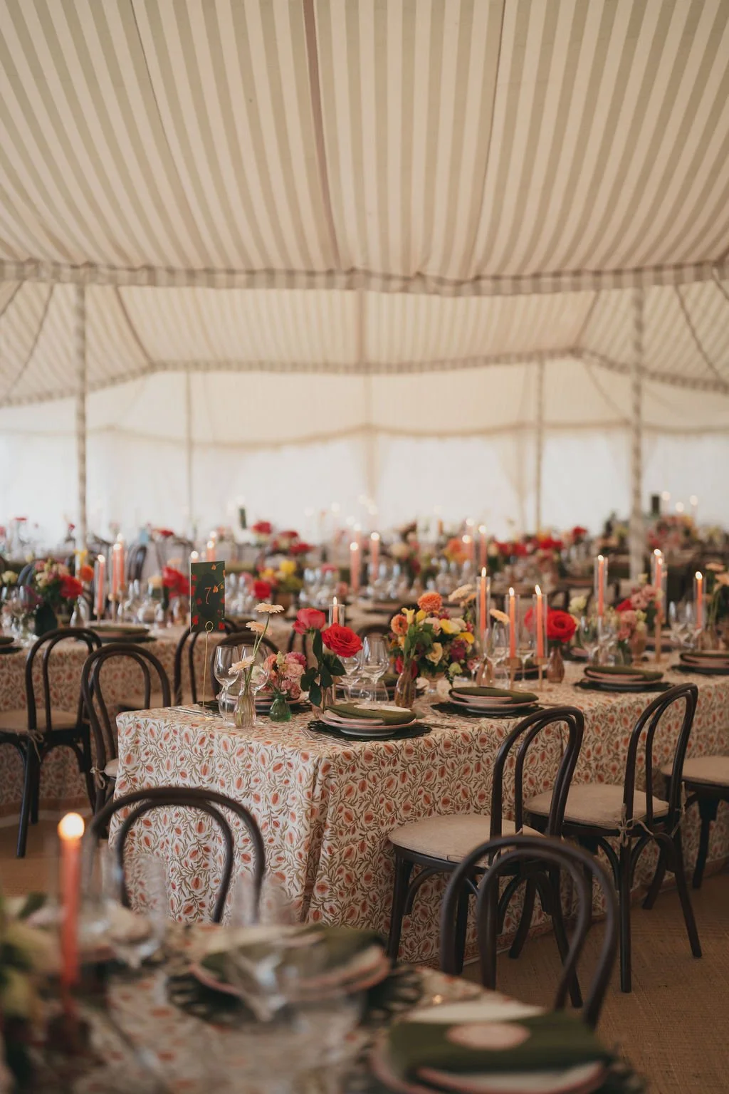 Decorated banquet tables with floral arrangements, candles, and place settings inside a large marquee at Kin House. 
