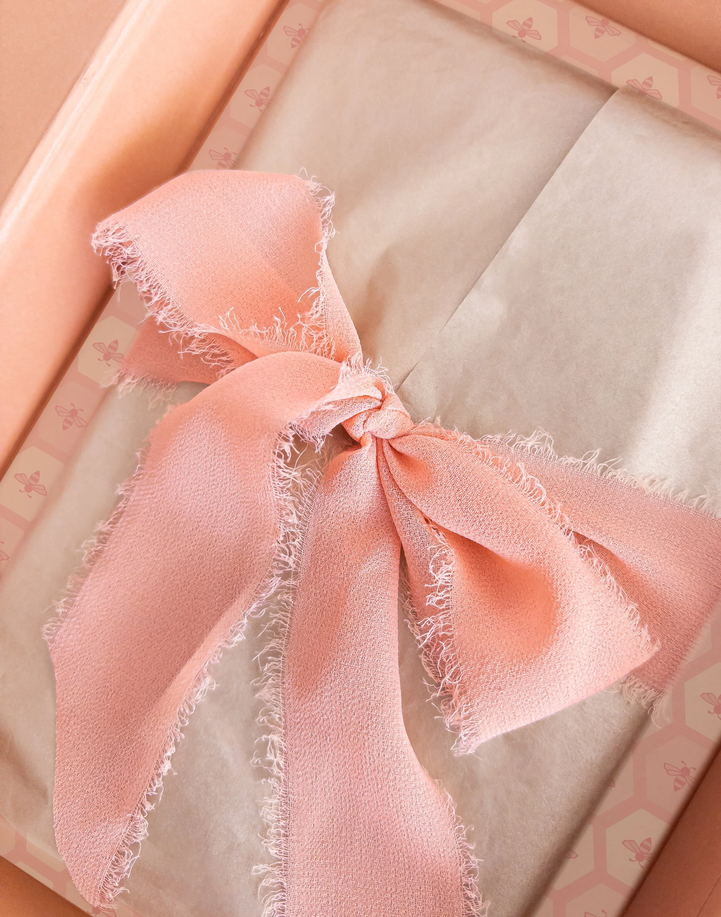 A pink gift box decorated with a large pink ribbon tied in a bow, with tissue paper inside.