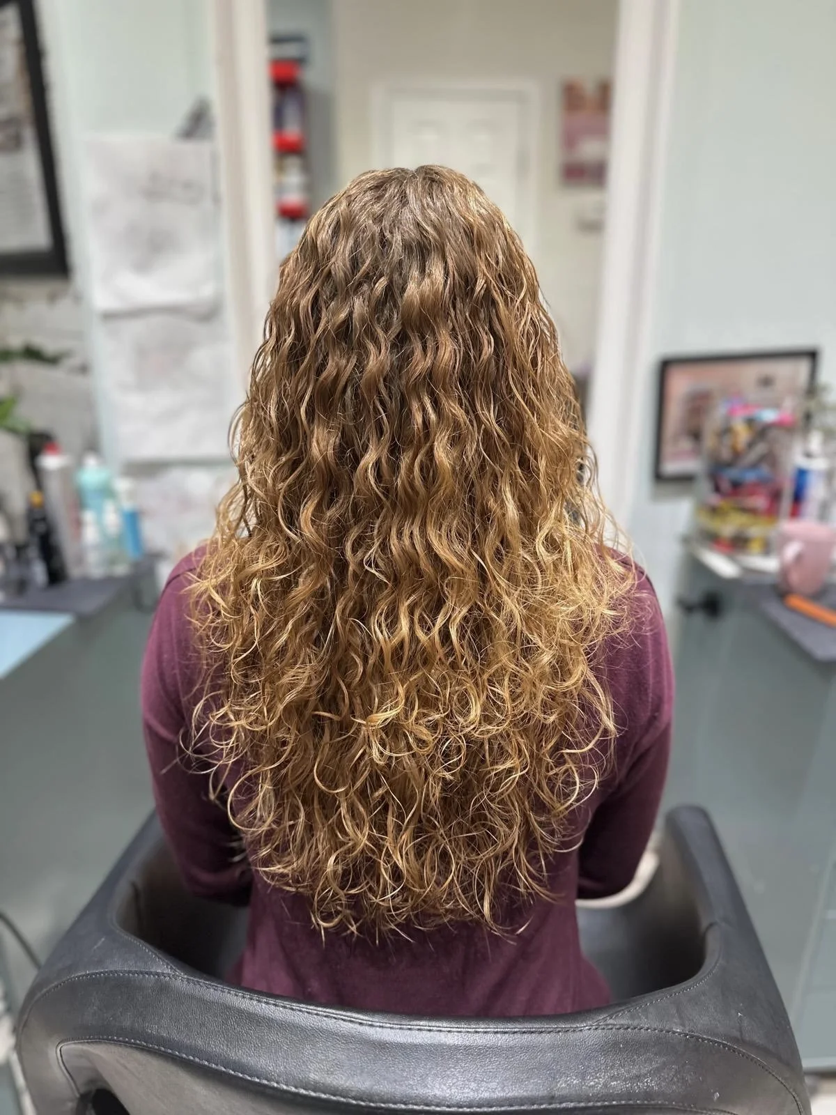 Back view of a client with long, glossy, wavy auburn hair in a salon chair