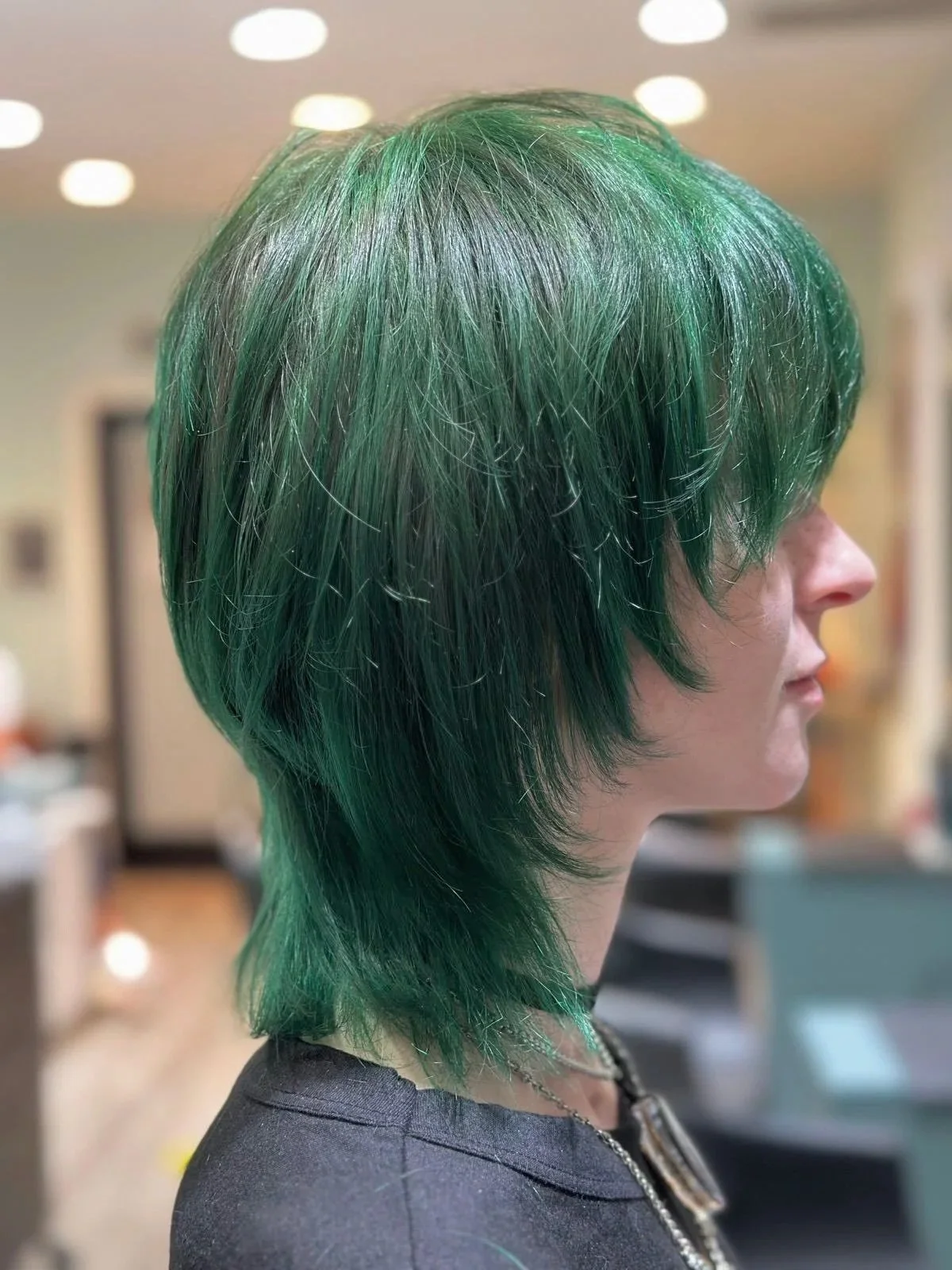 Side profile of a person with layered, shaggy green hair in a salon