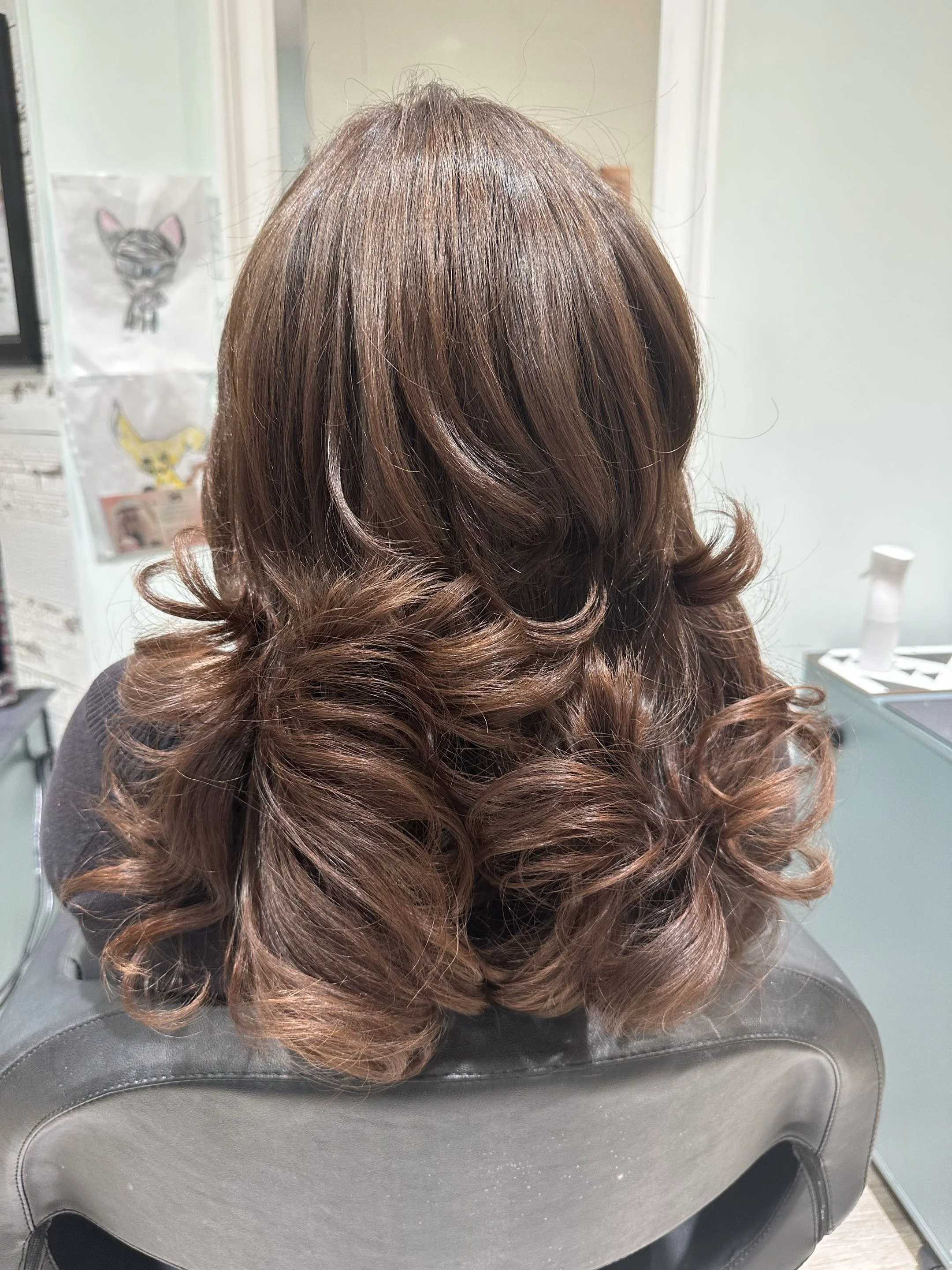 Back view of shoulder-length softly curled brown hair in a salon chair