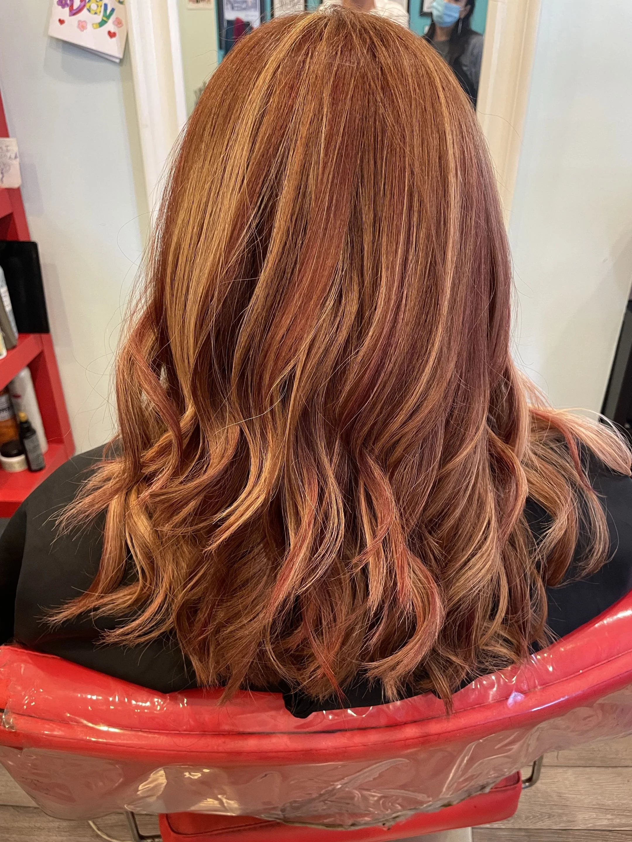 Back view of long, wavy auburn hair with copper highlights in a red salon chair