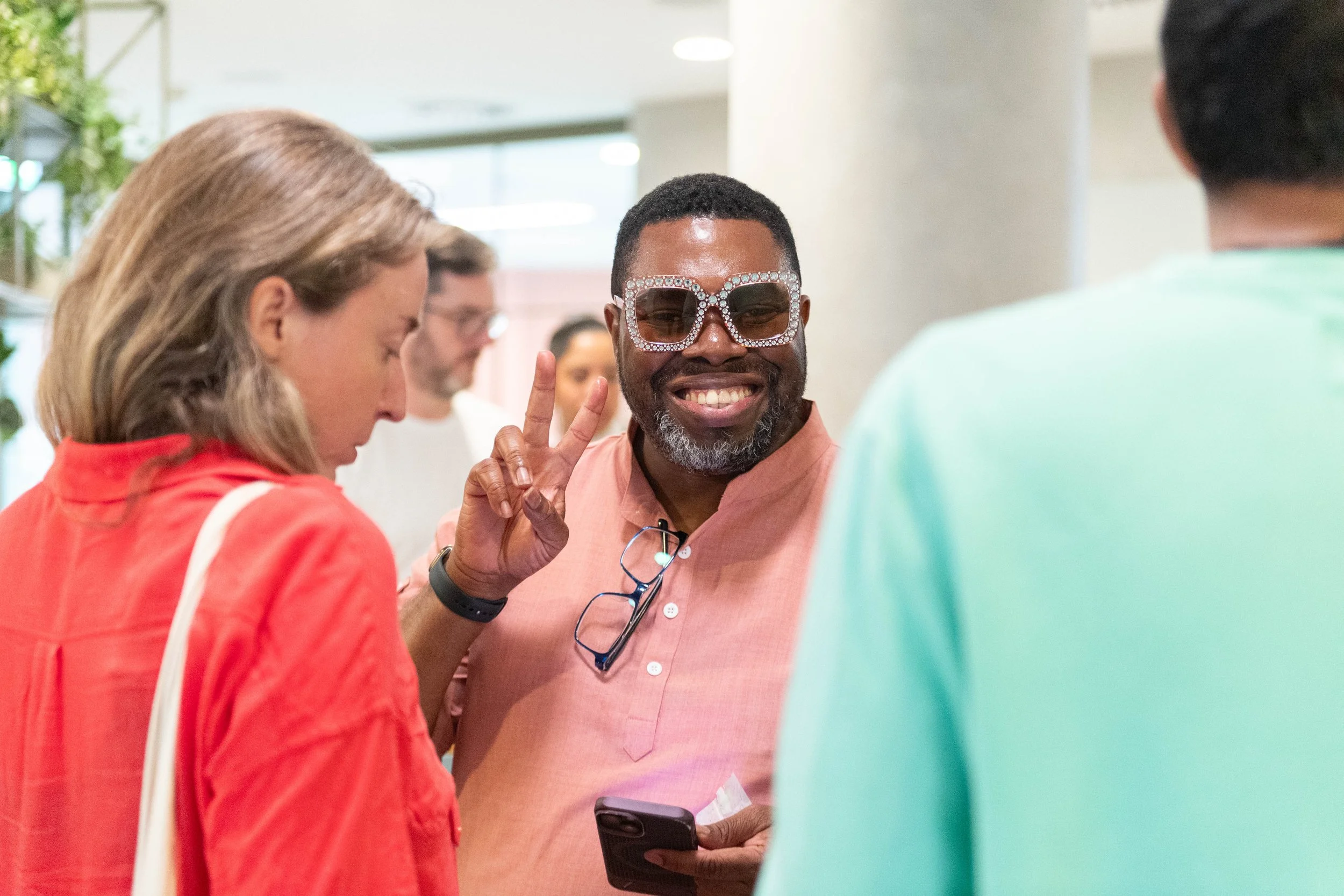 A networking attendees wearing sparkly sunglasses smiles at the camera whilst showing the peace sign
