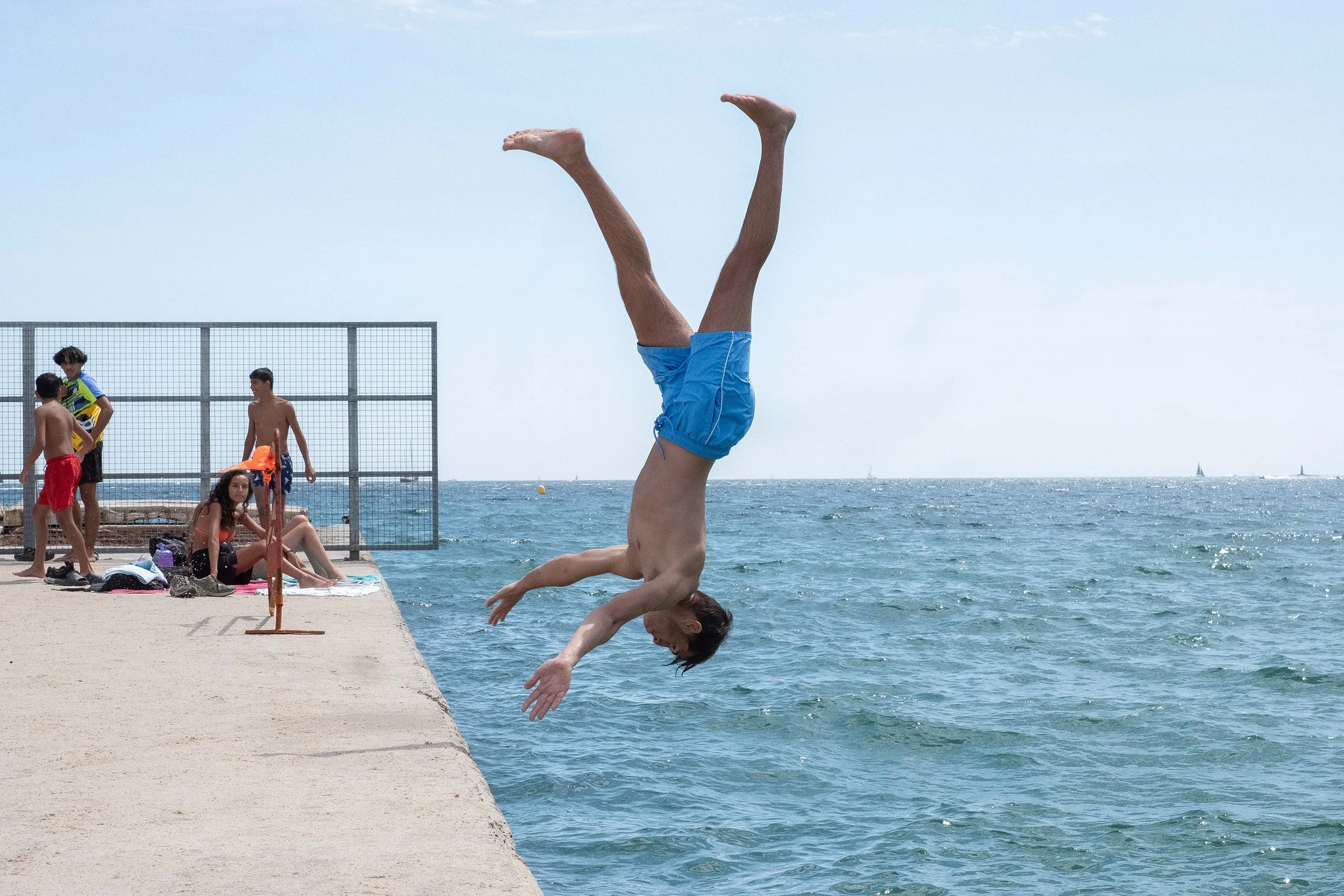 A group look on as a boy is captured in mid air (upside-down) before diving into the water