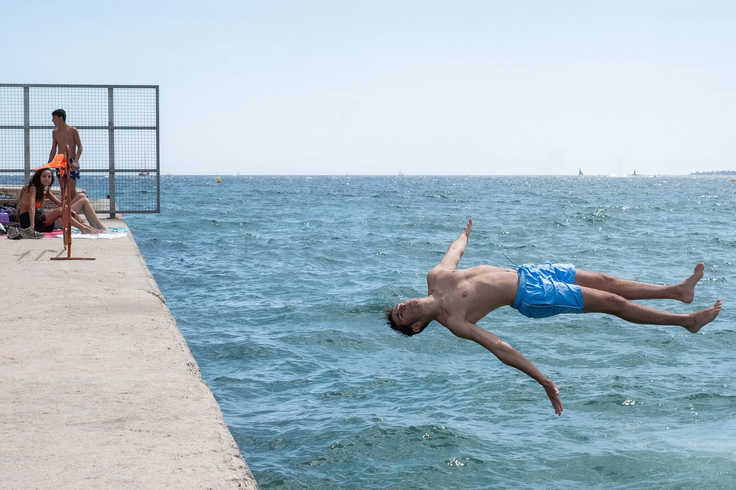 A group look on as a boy is captured in mid air (lying horizontal) before diving into the water