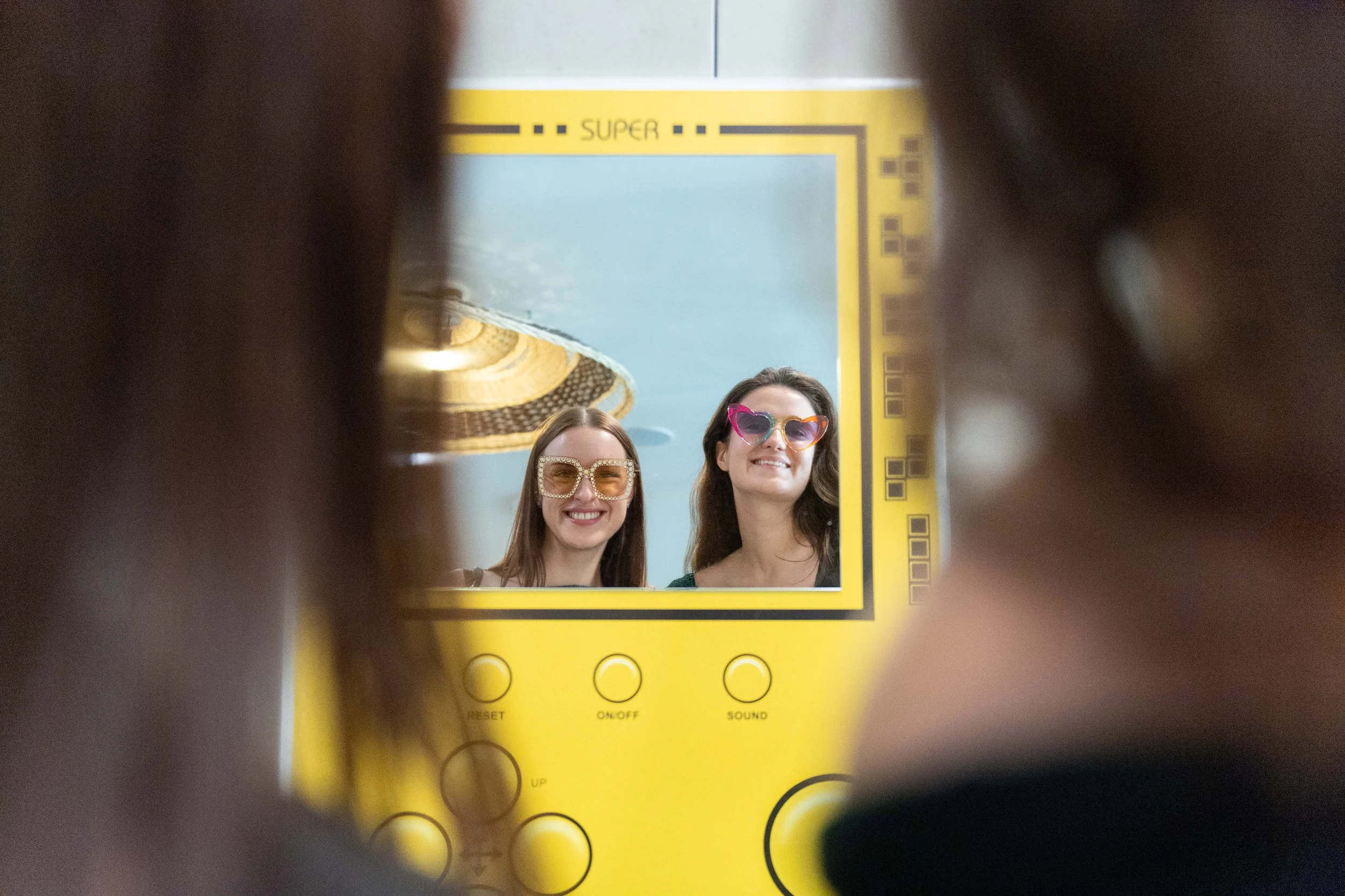 Two women wear sparkly sunglasses smile at their reflection in the mirror