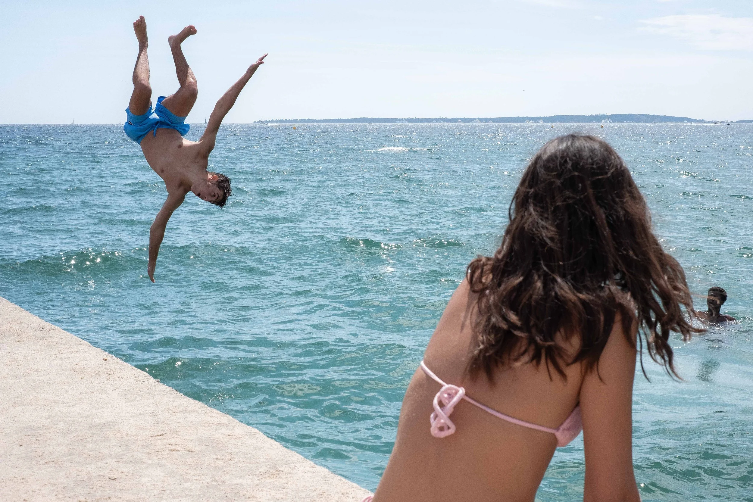 Girl looks on as boys somersaults into the water