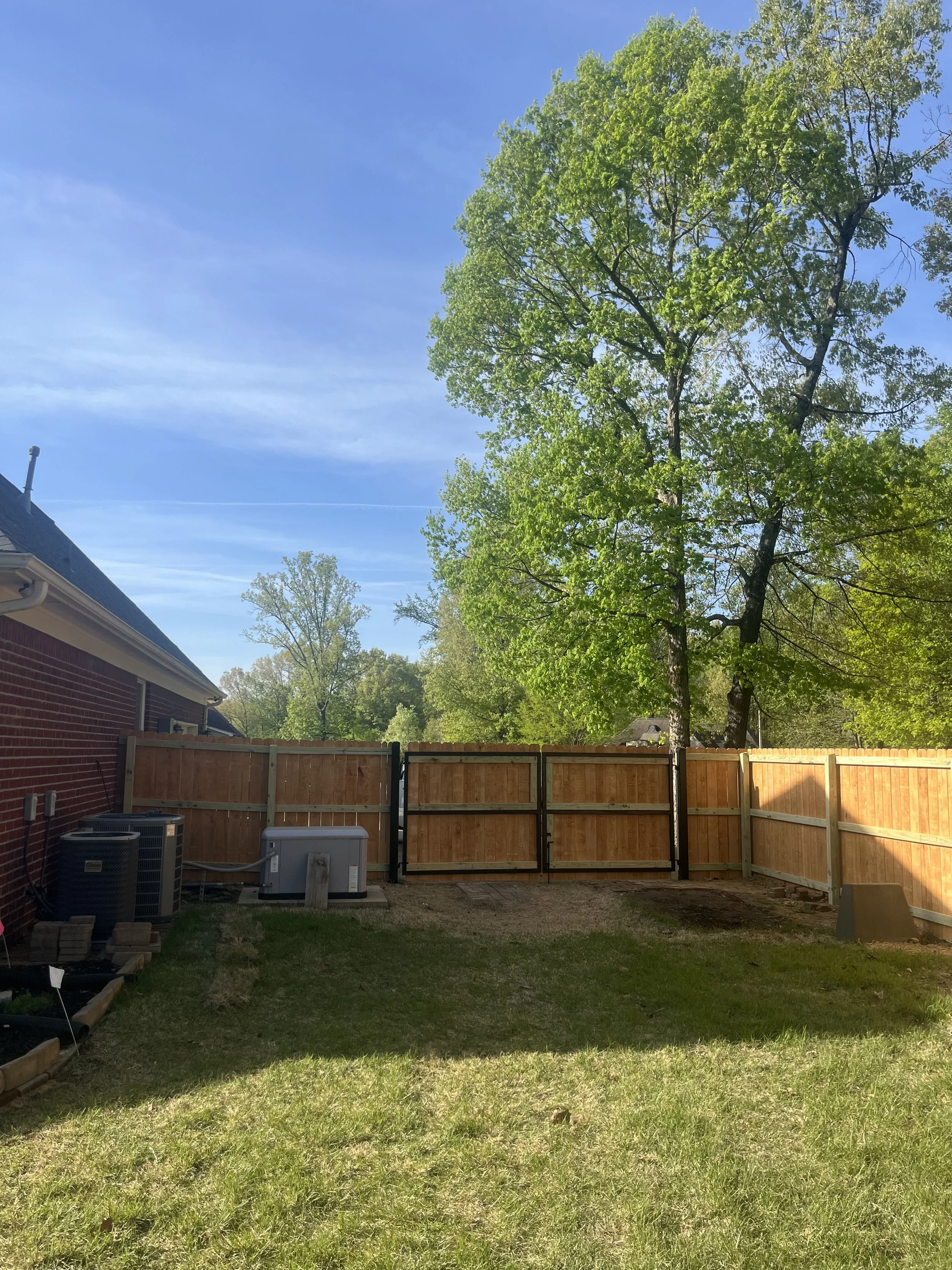 Steel-framed double cedar driveway gate installed with a cedar privacy fence at a residential property in Hernando, Mississippi.