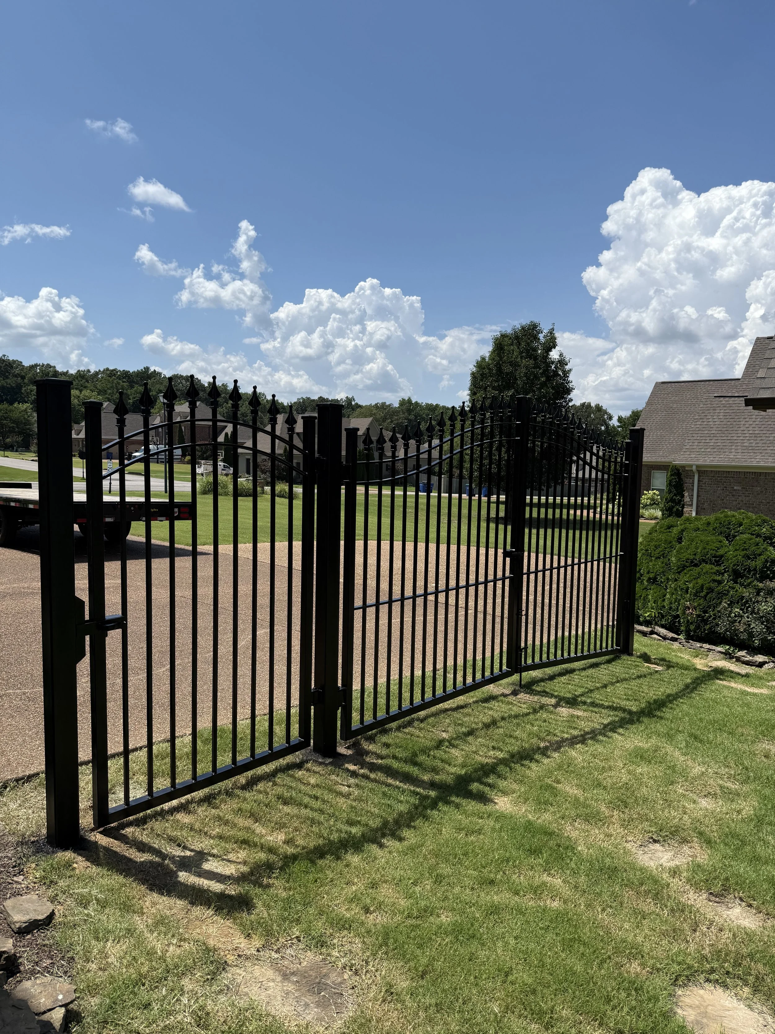 Angled view of a custom double spear-top steel driveway gate with matching ornamental fencing in Olive Branch, Mississippi by DeSoto Fence Co.