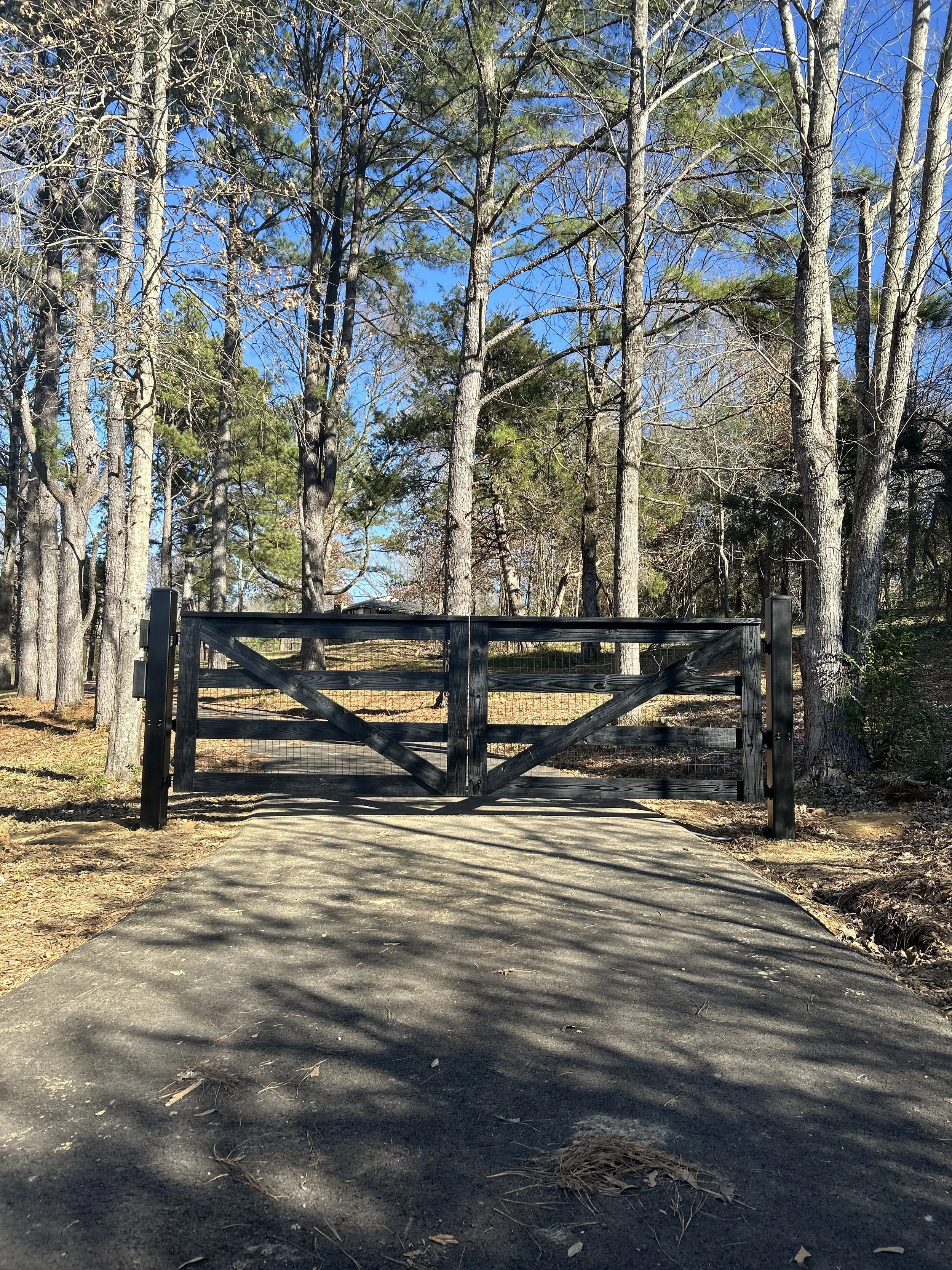Custom black stained crossbuck driveway gate with automatic gate opener installed at a residential property in Hernando, Mississippi.