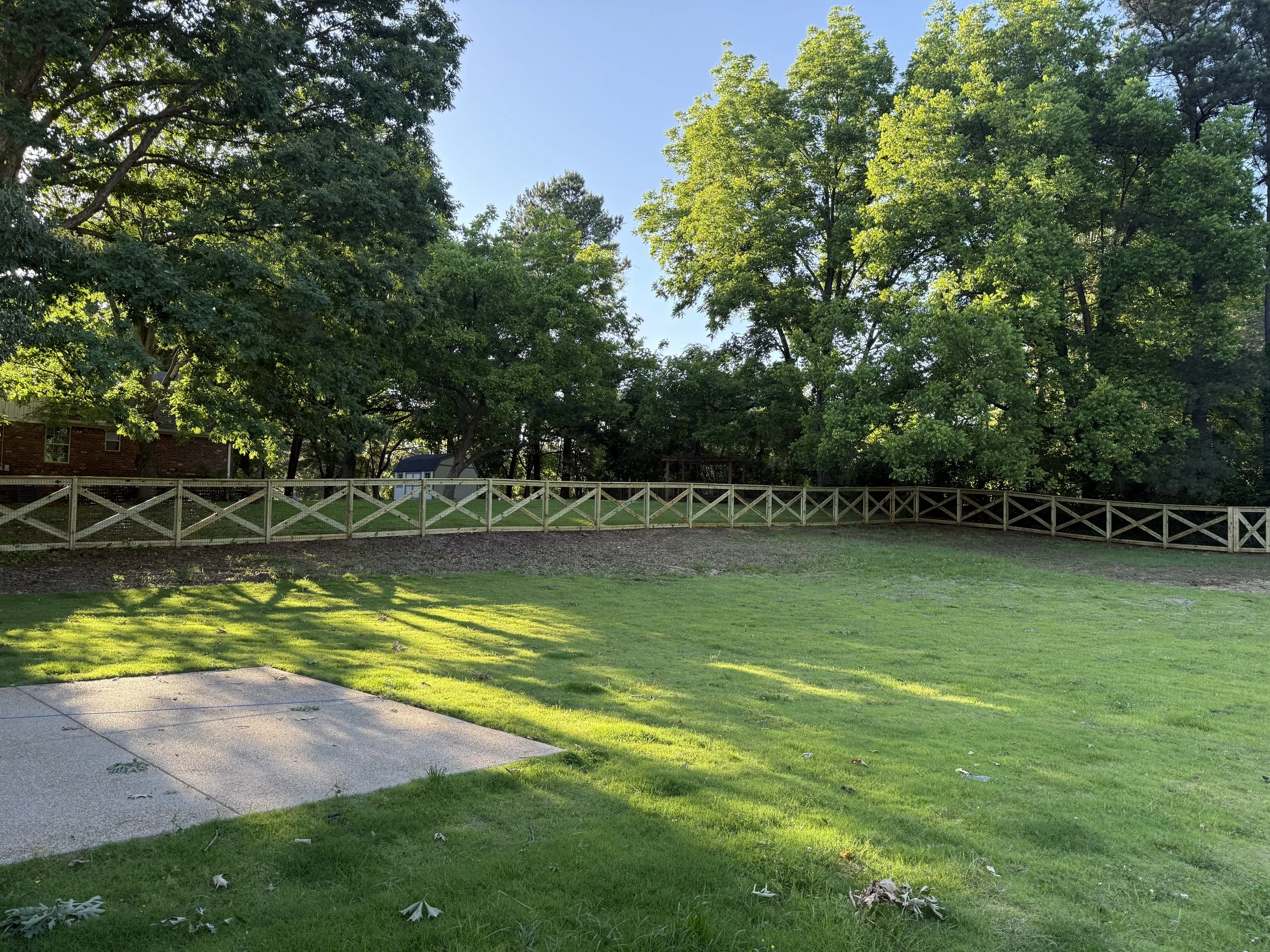 Wide view of a crossbuck fence with black wire enclosing a large backyard in Olive Branch, MS. The long run highlights consistent spacing and straight fence lines across the property.