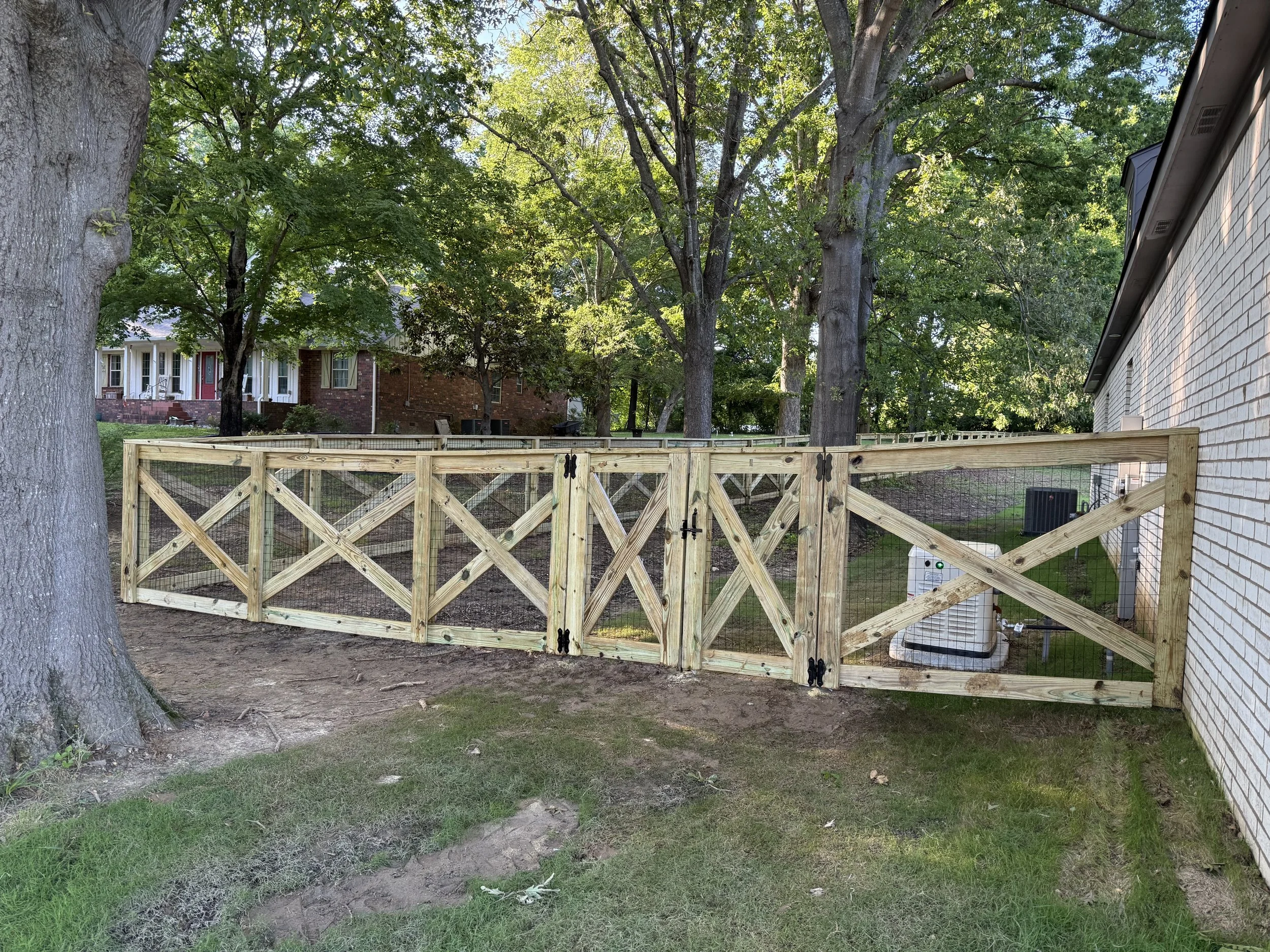Custom crossbuck fence with black wire and double gate installed in Olive Branch, MS. This section shows the framed X-pattern design with heavy-duty hinges and a clean gate tie-in.
