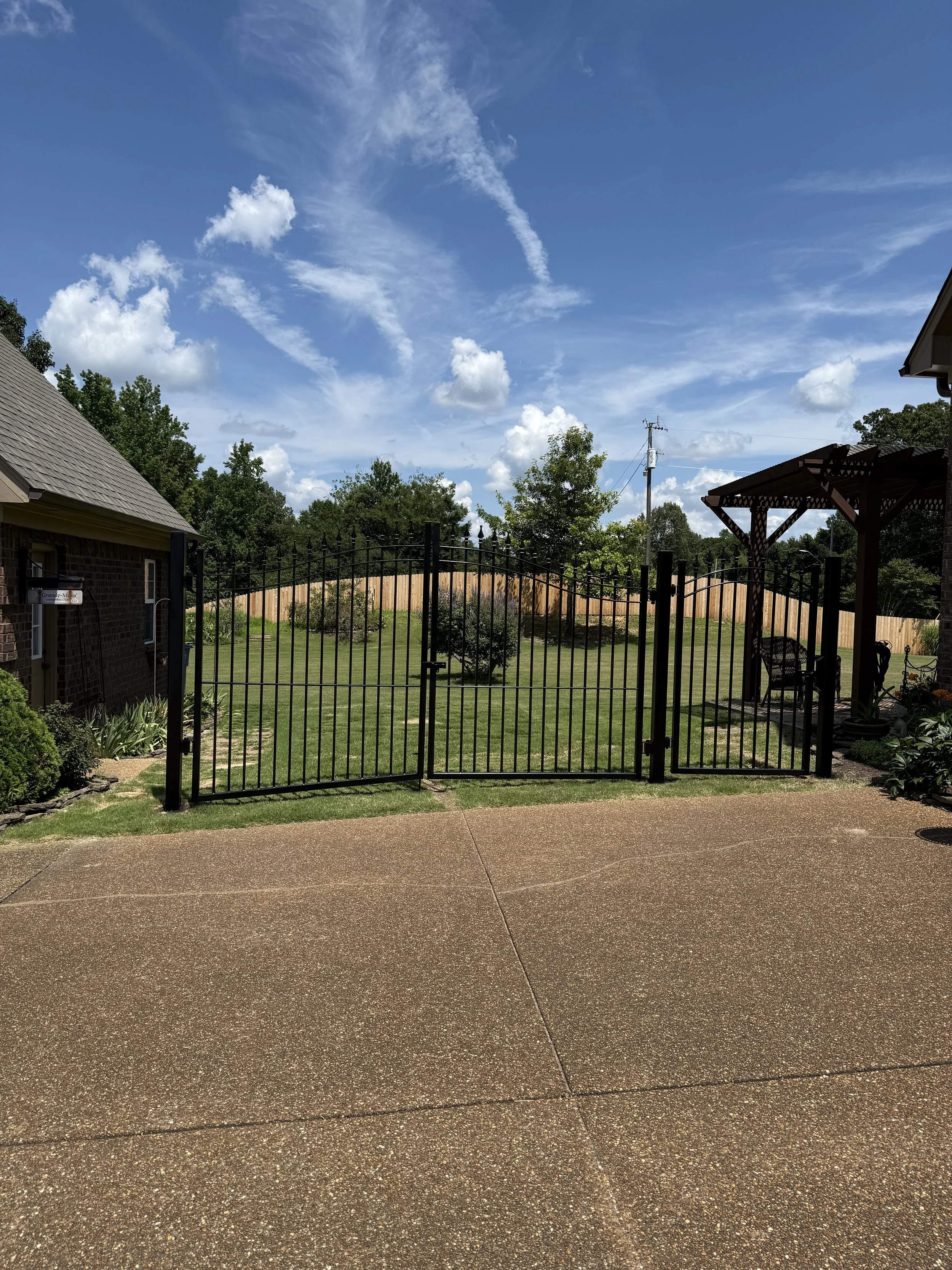 Double spear-top ornamental steel driveway gate with a matching walk gate installed at a residential property in Olive Branch, Mississippi by DeSoto Fence Co.