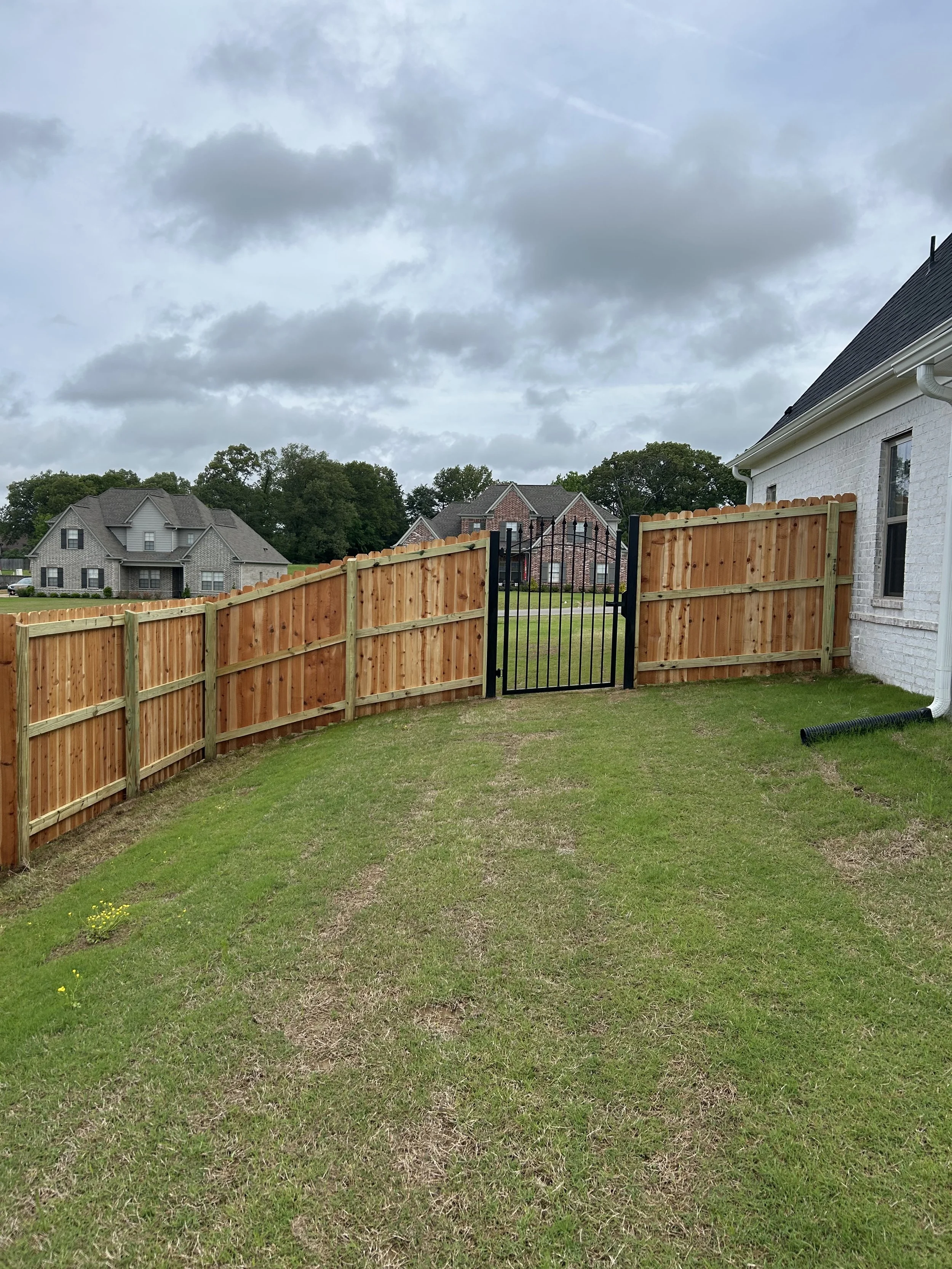 Rear view of an ornamental steel walk gate installed with a cedar privacy fence on a sloped property in Southaven, Mississippi by DeSoto Fence Co.