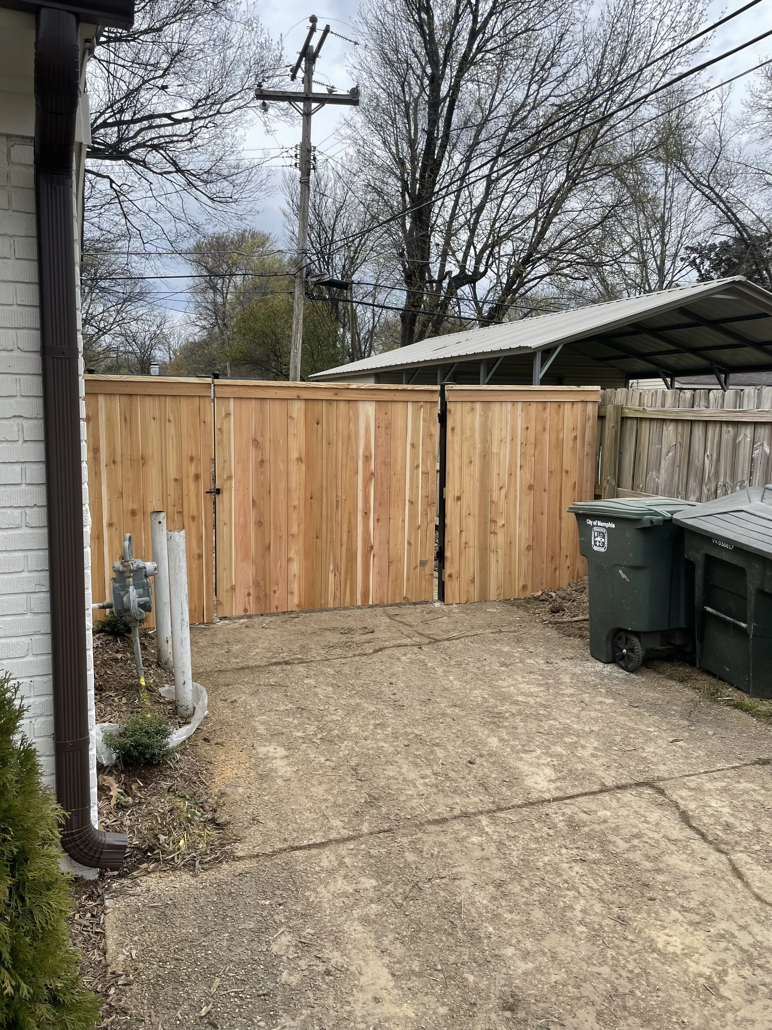 Backyard with a newly installed wooden fence, concrete patio, garbage bins, and a power meter on the house wall.