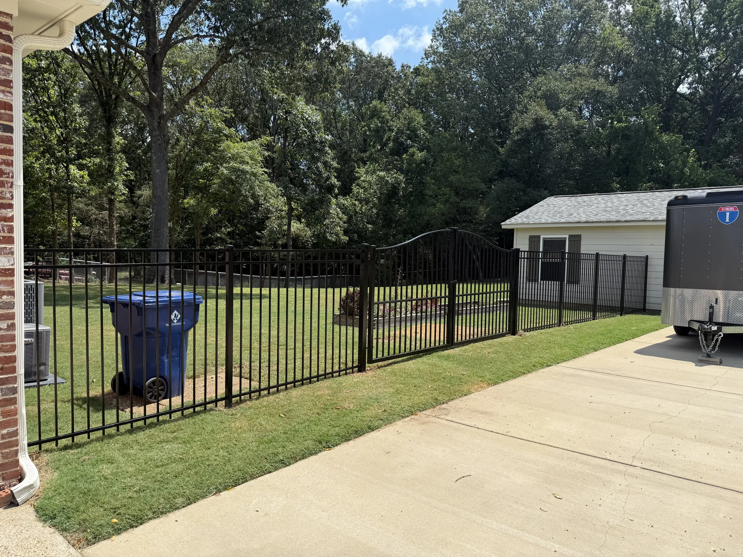 Angled view of a custom arched aluminum driveway gate with matching residential fencing installed in Hernando, Mississippi by DeSoto Fence Co.