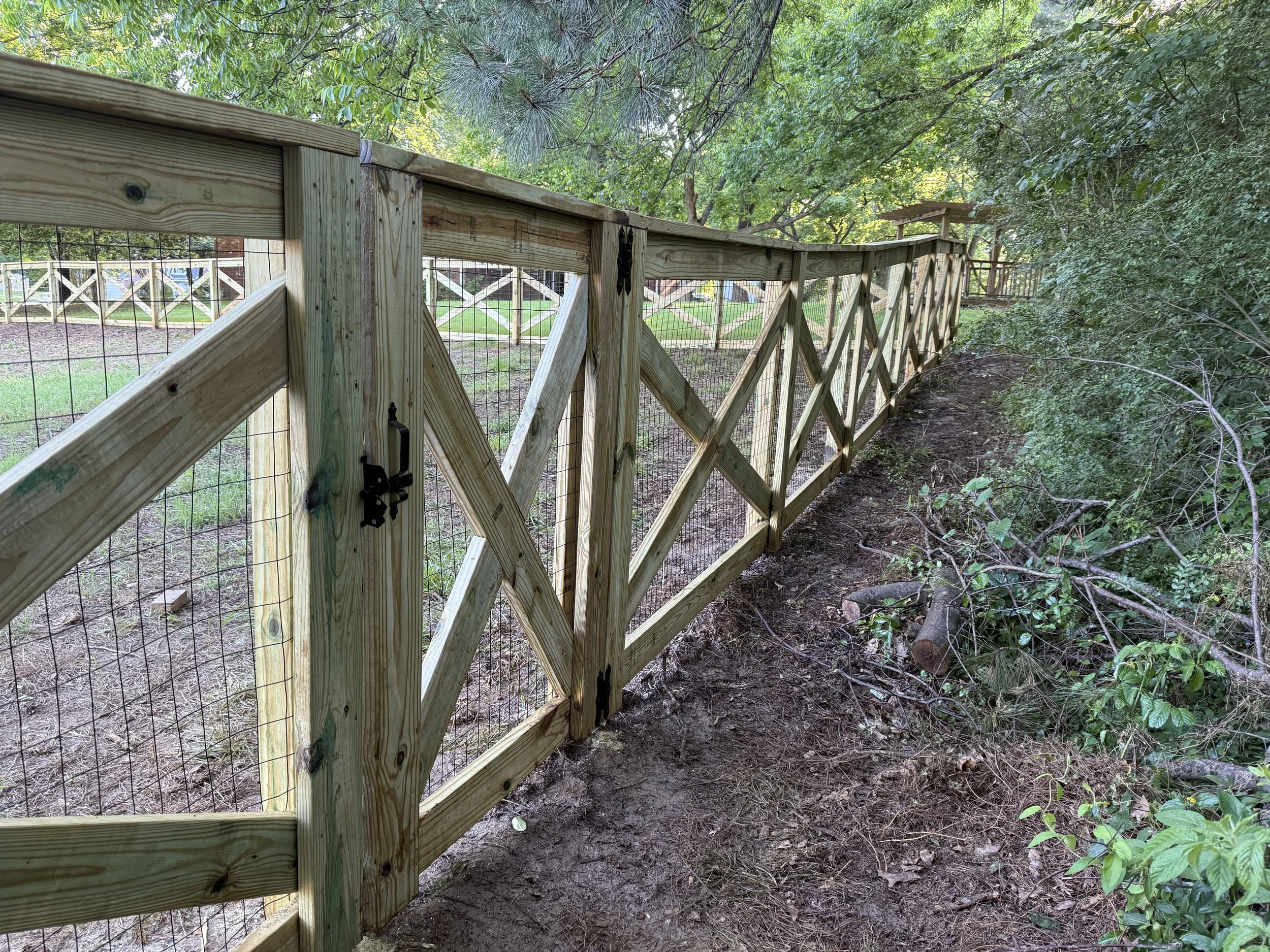 Crossbuck fence with black wire installed along a wooded property line in Olive Branch, MS. This angle shows how the fence follows the terrain while maintaining a clean, uniform layout.