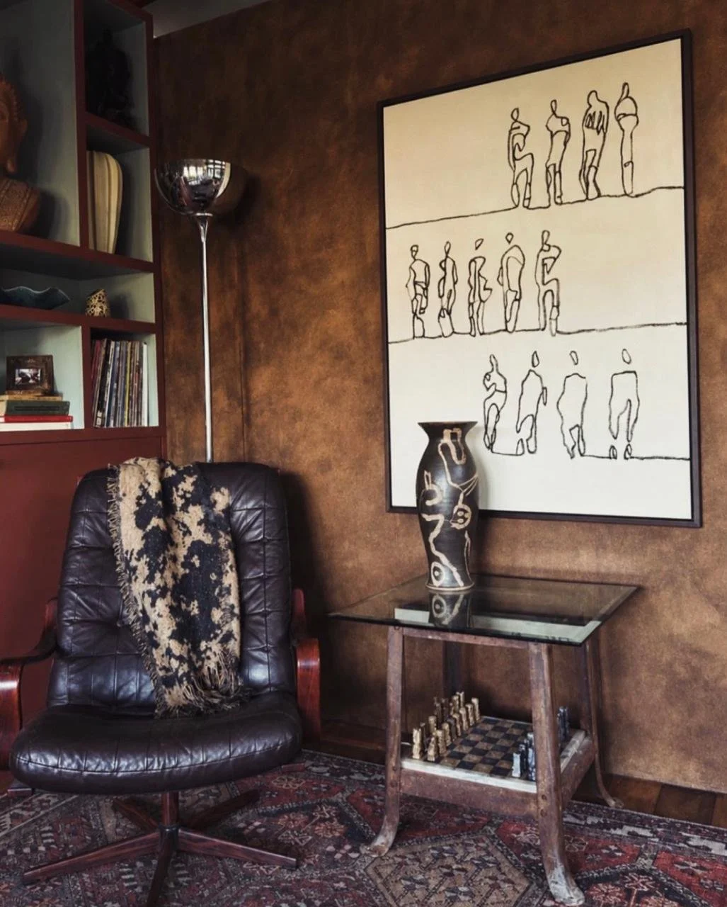 A cozy living room corner featuring a leather arm chair with an abstract line drawing by artist Lili Dauphinee hanging on the wall behind it.