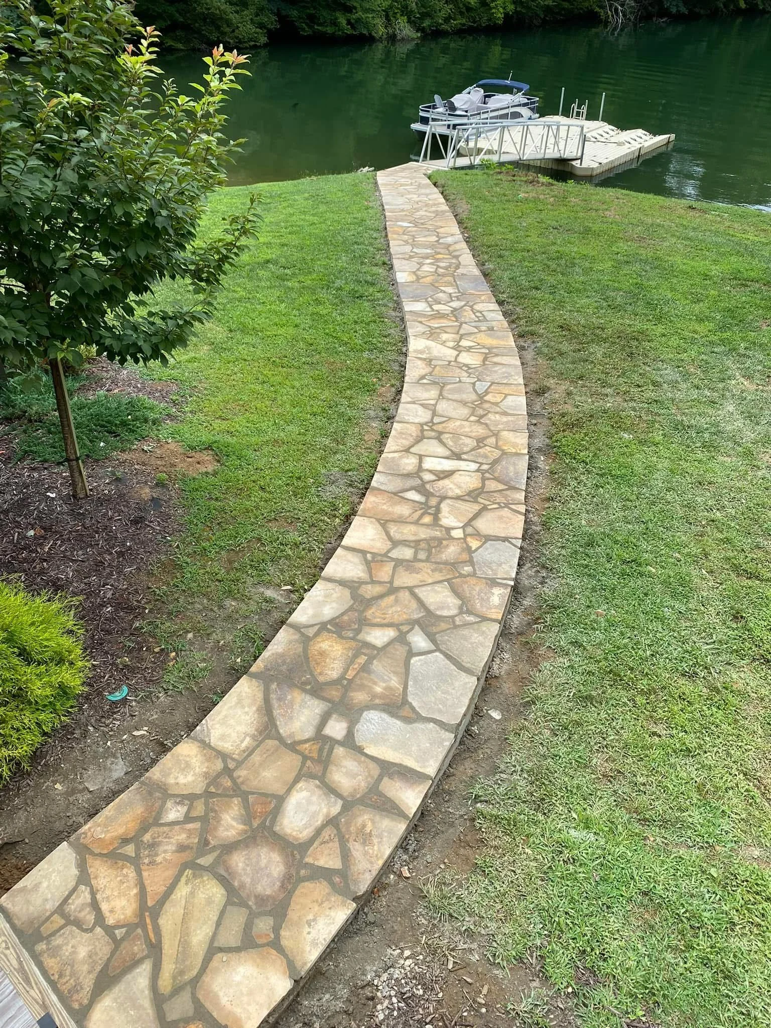 Progress on a stone sidewalk leading to a set of stairs with brick risers, in front of a house with stone and siding exterior.