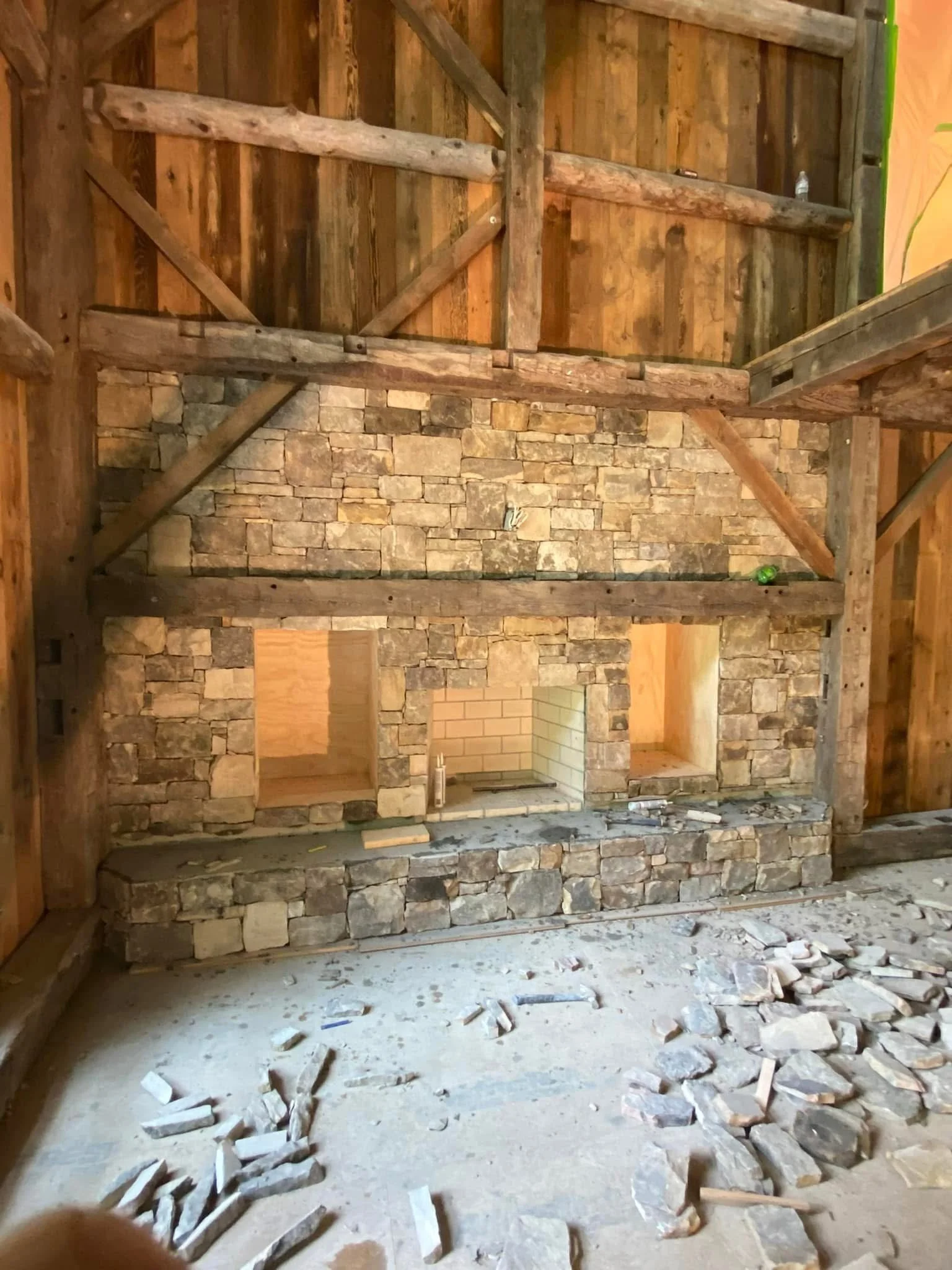 Interior of a room with a stone fireplace, large ceiling fan, and two glass double doors leading outside.