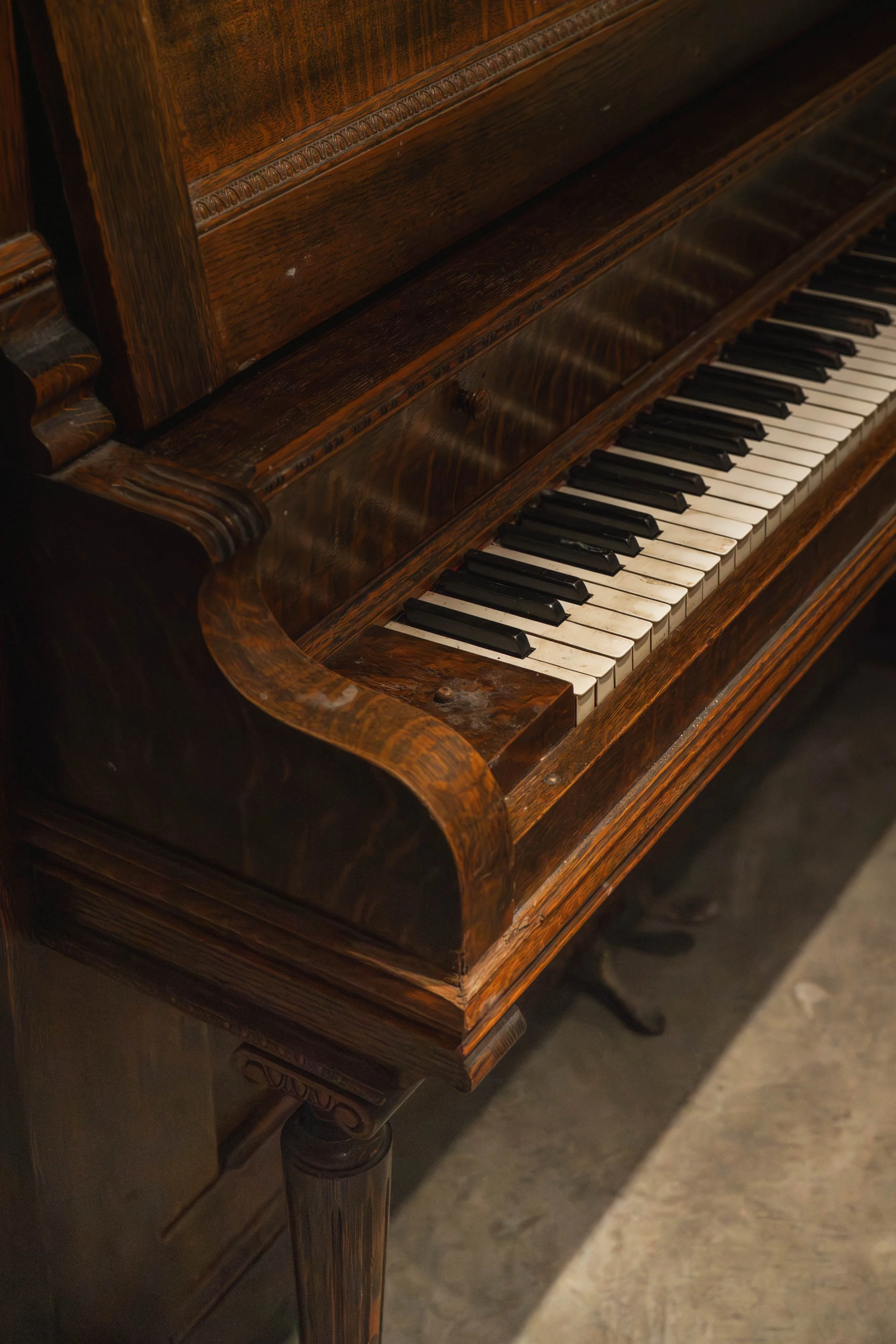 Close-up of an antique wooden piano with slightly worn keys, showing dark brown polished wood and some minor damage on the keys and wood.