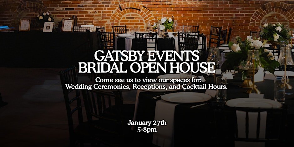 Interior of an event space with round tables decorated with white tablecloths, floral centerpieces, and black chairs. Brick wall in the background with arched accents.