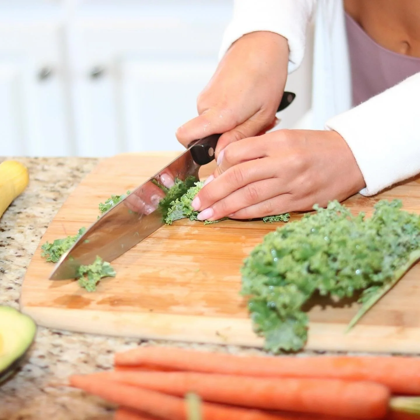 Person chopping kale on a cutting board in a kitchen.