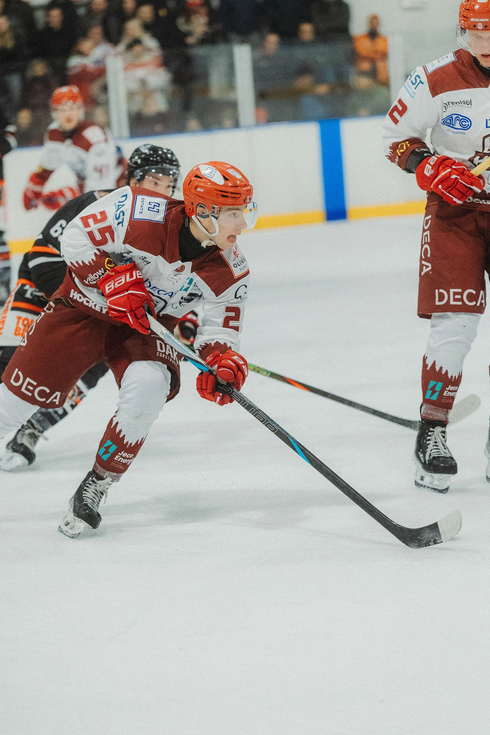 Hockey players in red and white jerseys competing on ice rink with spectators watching in the background.