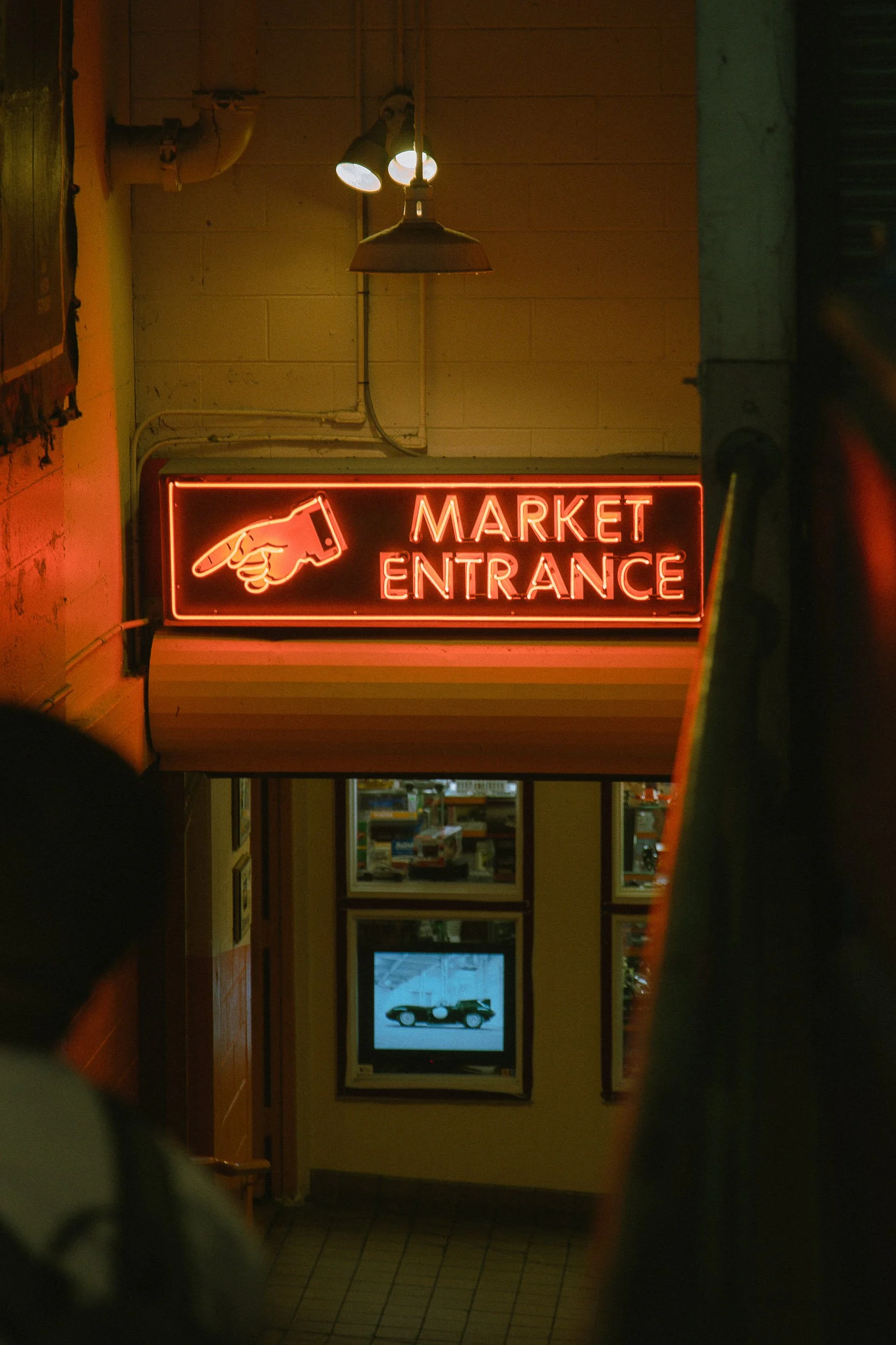 Neon sign reading 'Market Entrance' with a pointing hand icon above the entrance of a store.