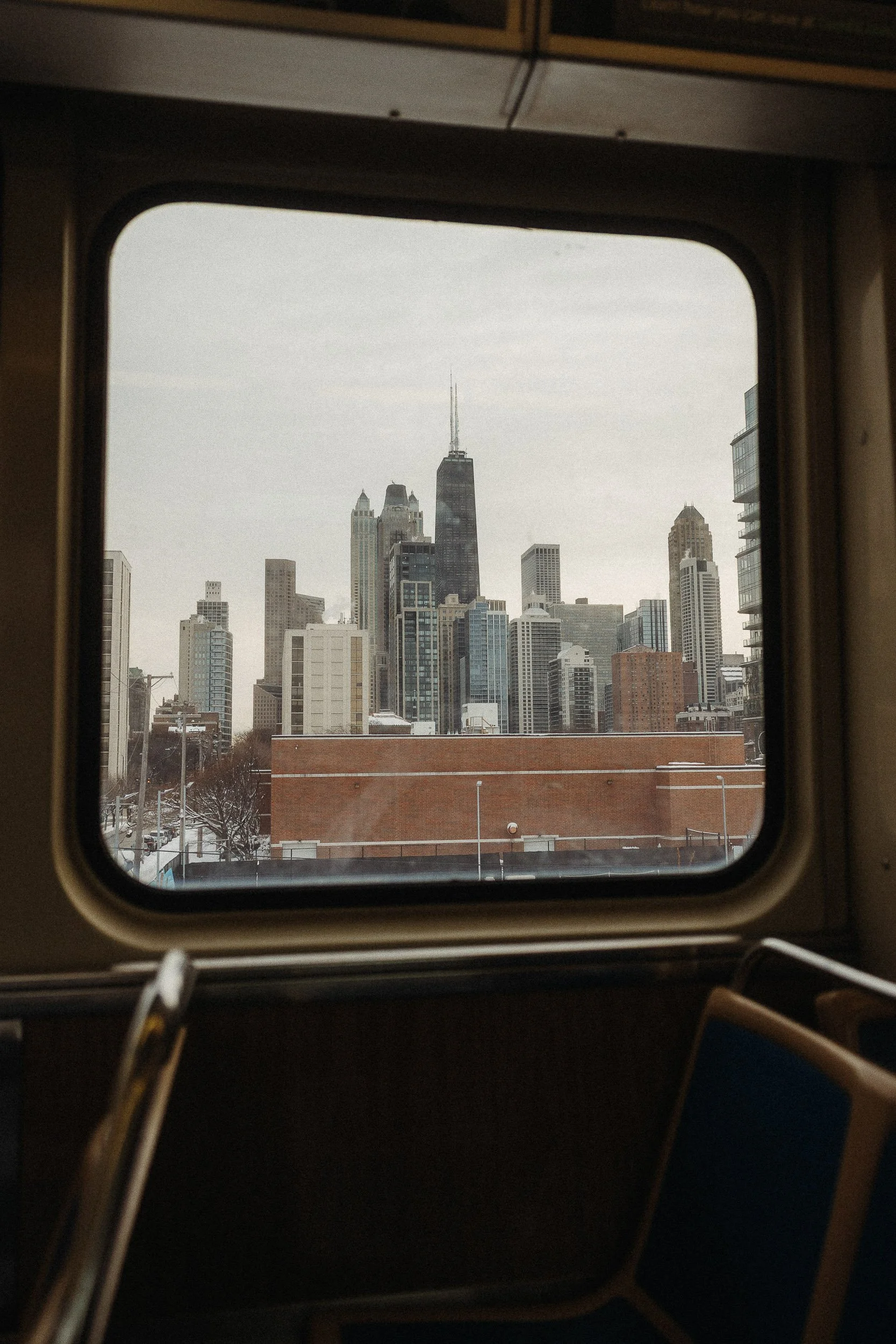 City skyline seen through a window of a bus or train, with tall buildings and skyscrapers, including the tallest one in the center.