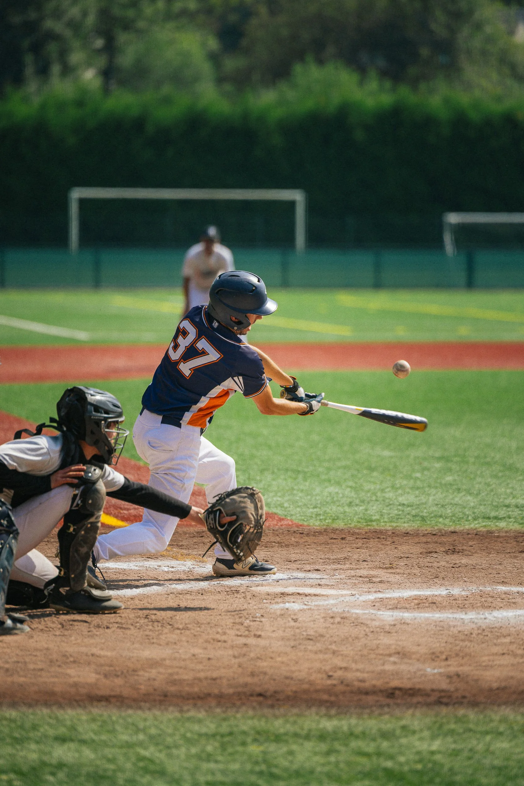 A baseball player wearing a navy blue jersey with the number 37 slides at home plate as the ball approaches during a game on a sunny day.