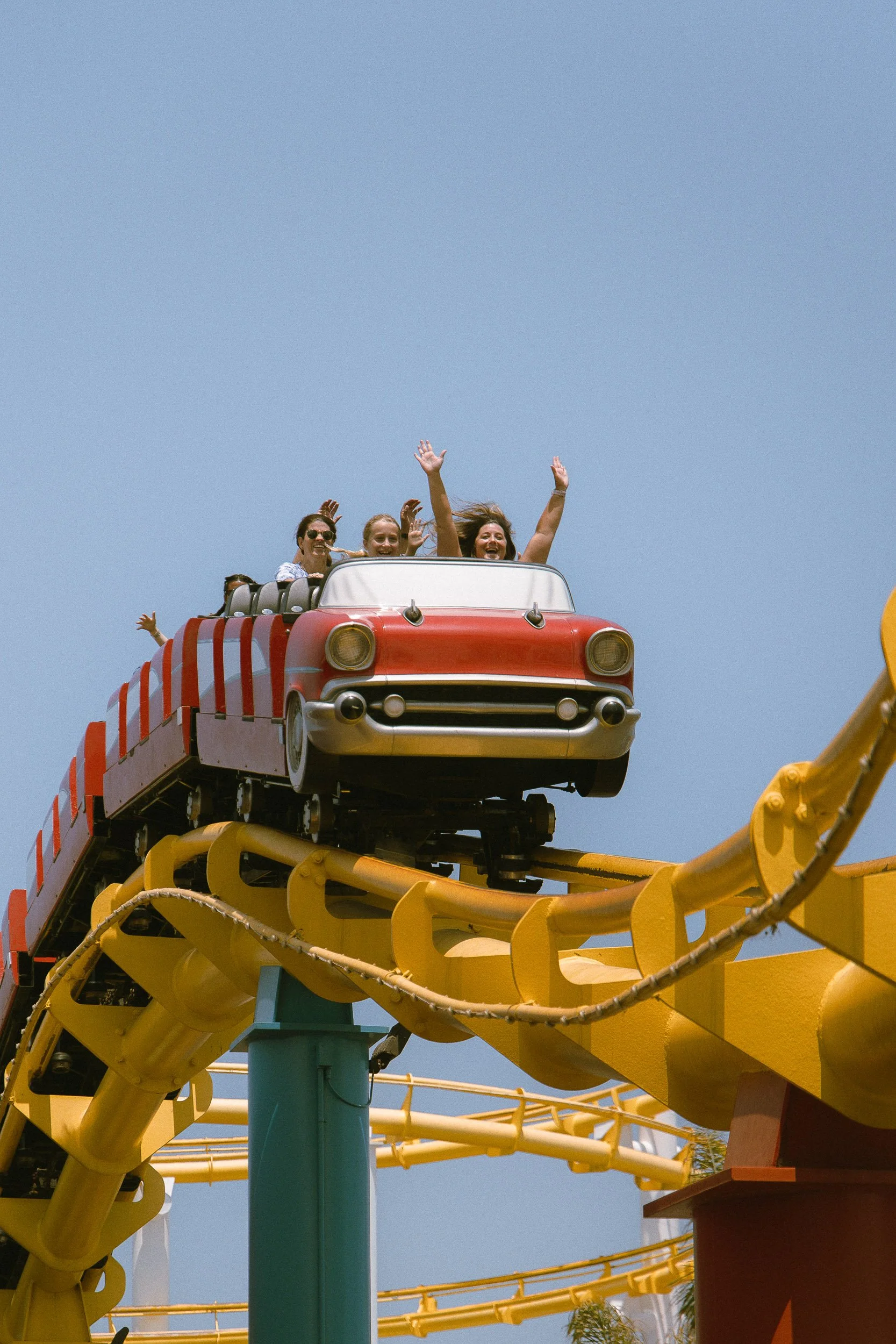 People enjoying a roller coaster ride in a small car at an amusement park, with a clear blue sky in the background.
