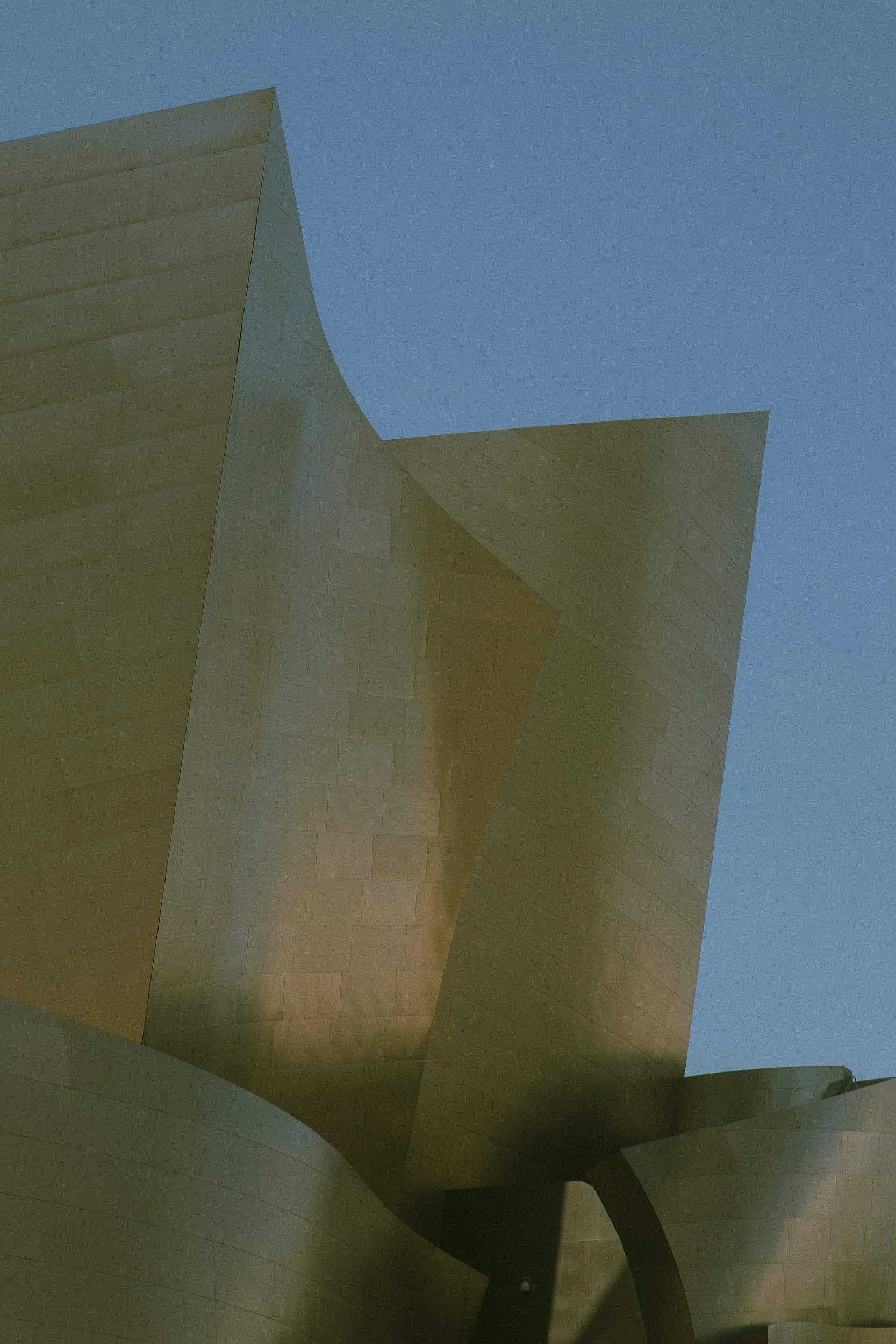 Close-up of a modern, gold-colored architectural building with curved and angular metal panels against a clear blue sky.