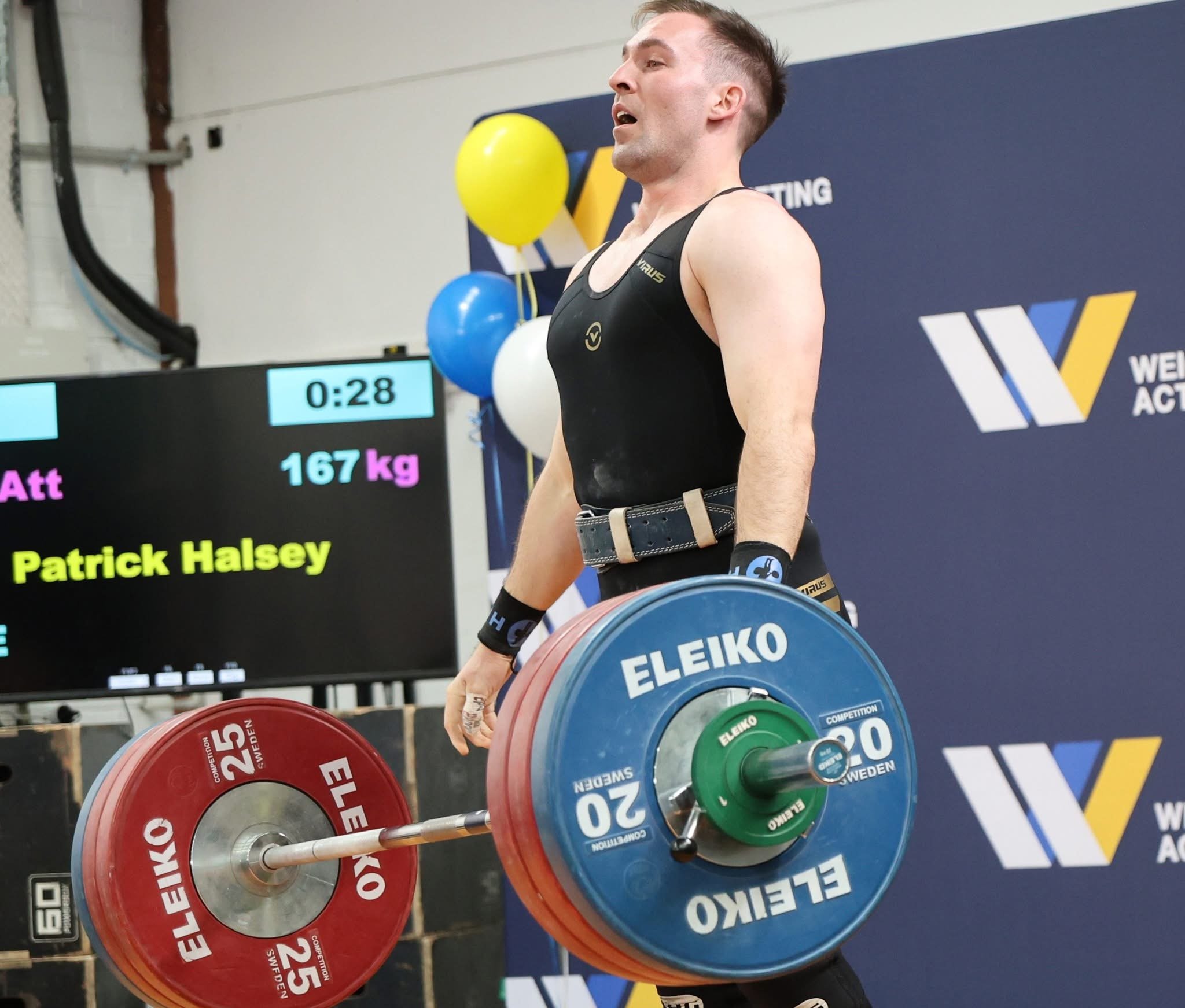 A male weightlifter in black attire performing a deadlift, lifting a barbell with red, green, and blue weights at a competition.
